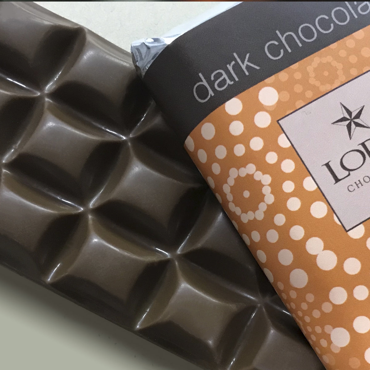 close up of Lore's Chocolates' Dark Chocolate Bar and the old orange chocolate wrapper