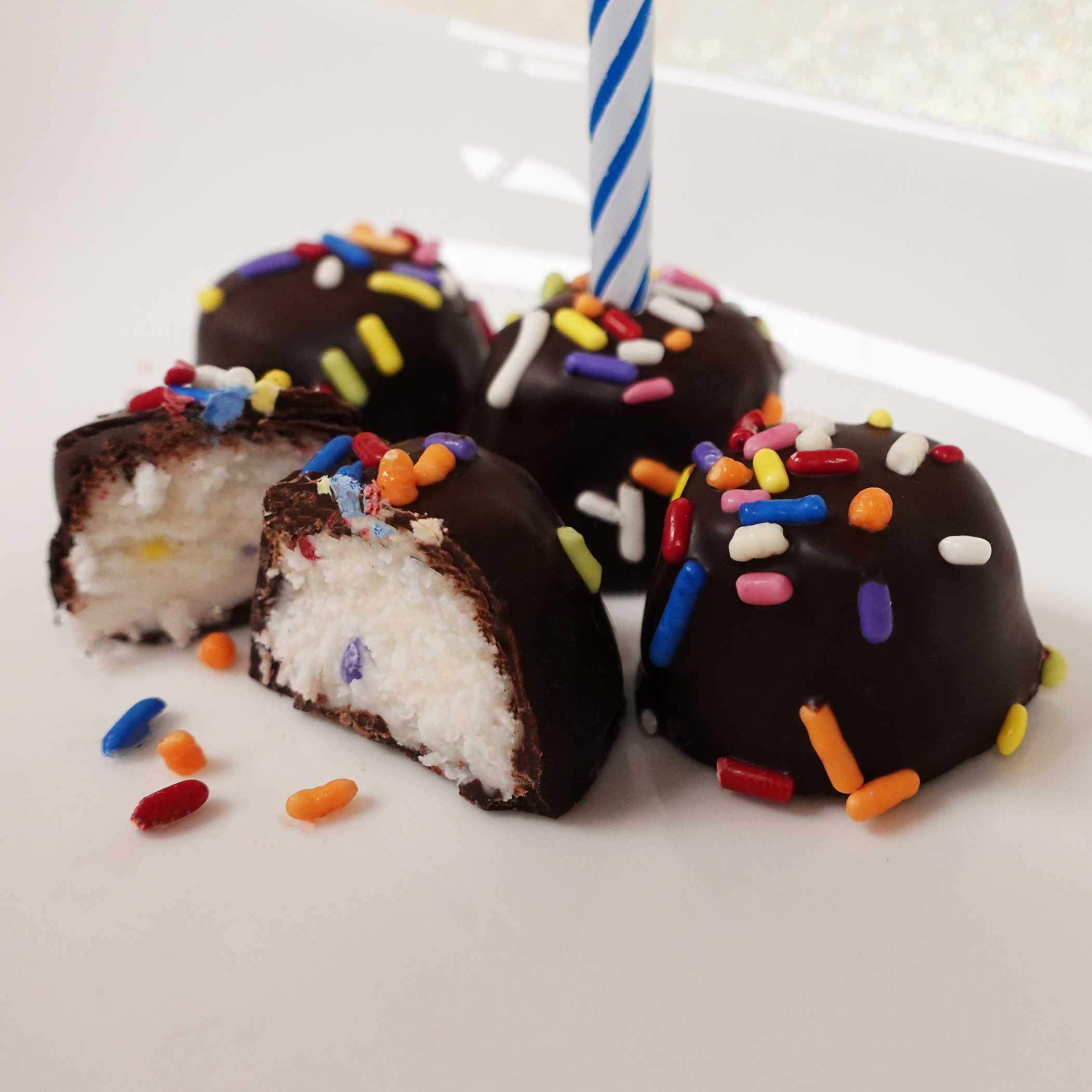 Dark Chocolate birthday cake butter creams with rainbow sprinkles. Image shows a birthday candle in one of the chocolates