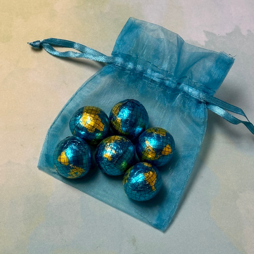 A set of solid milk chocolate globes with a blue and green foil exterior, contained within a blue organza bag with a blue ribbon.