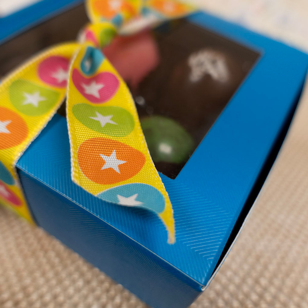 Blue box close up to detail box texture with a colorful easter egg star-patterned ribbon on a textured surface
