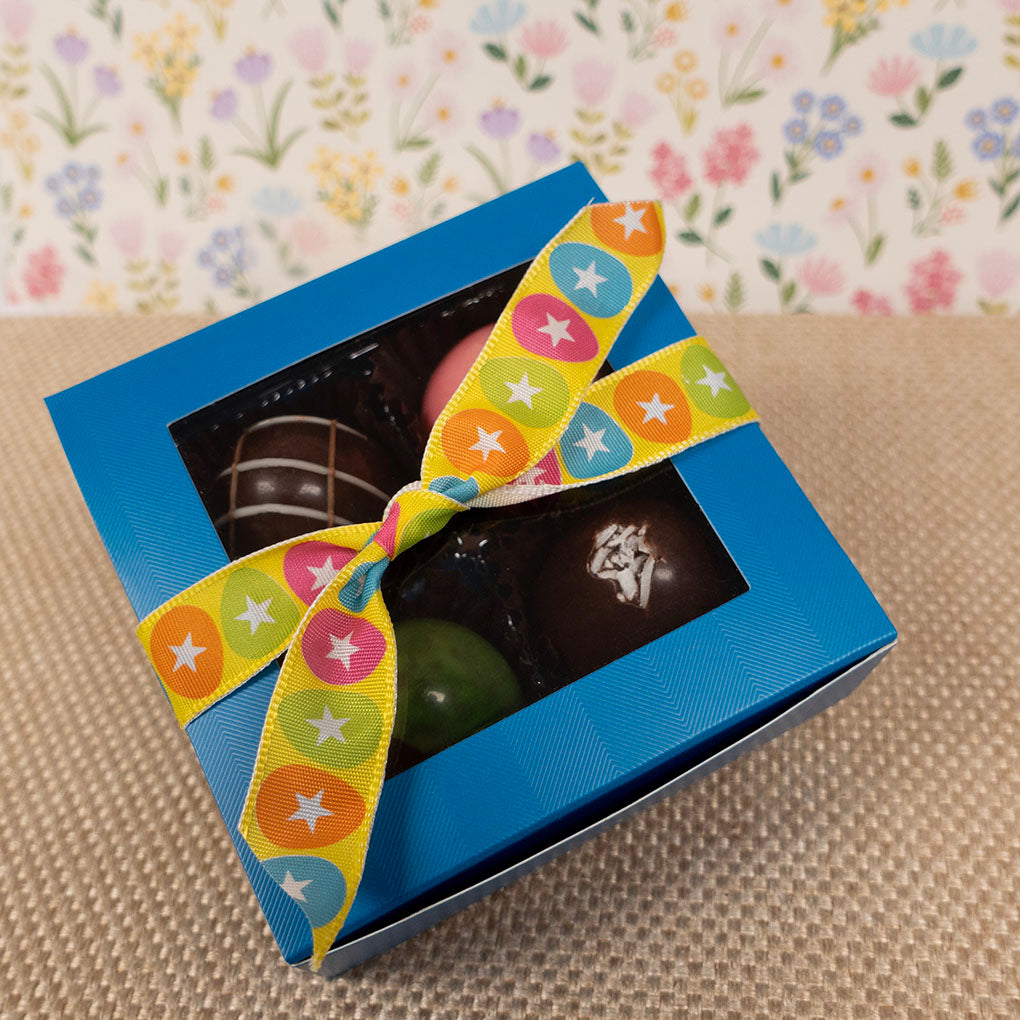 Blue gift box with 4 large chocolate truffles with a colorful ribbon on a textured surface with a floral-patterned background