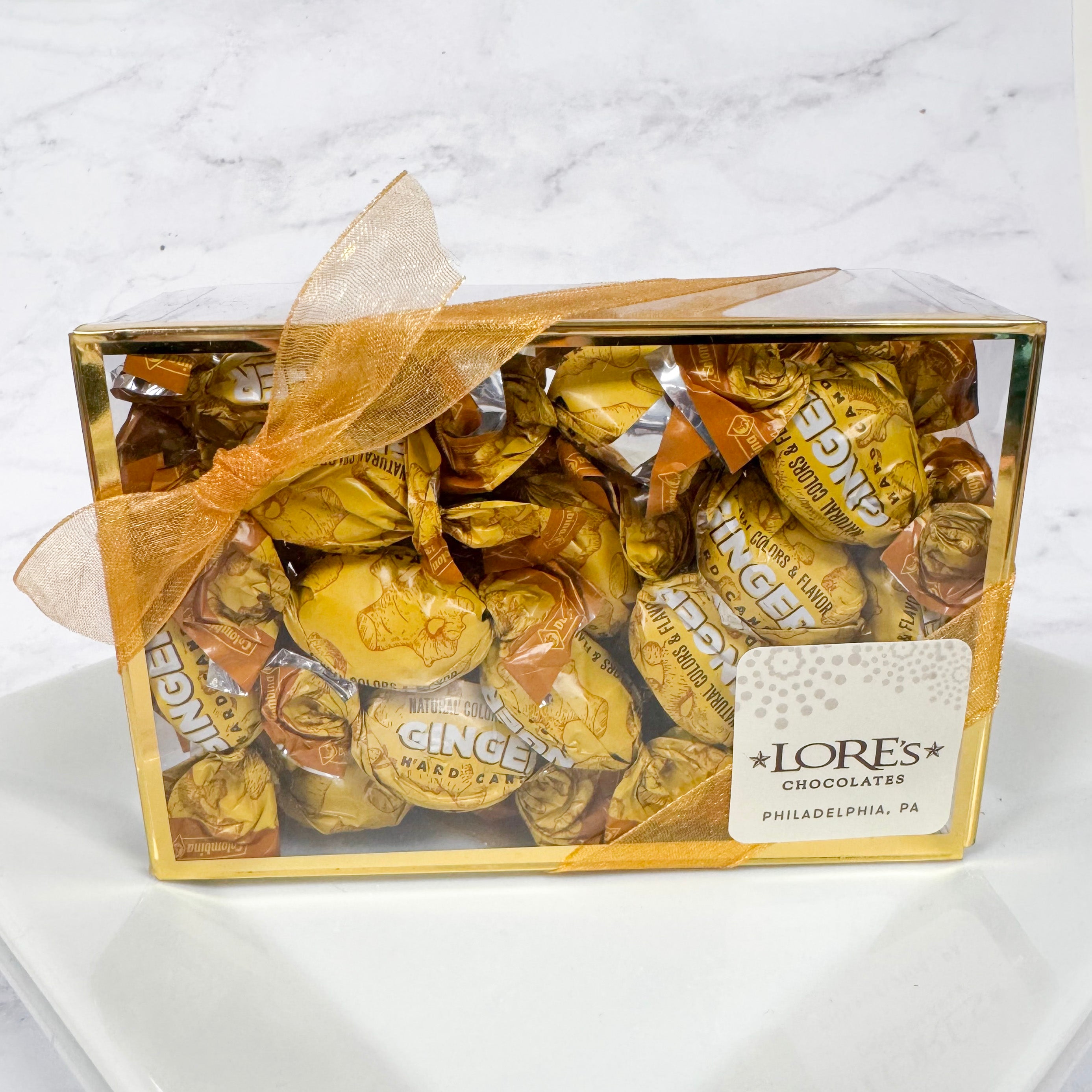 Ginger hard candies individually wrapped and packaged in a clear box with gold boarders. sticker reads "Lore's Chocolates in Philadelphia, PA"