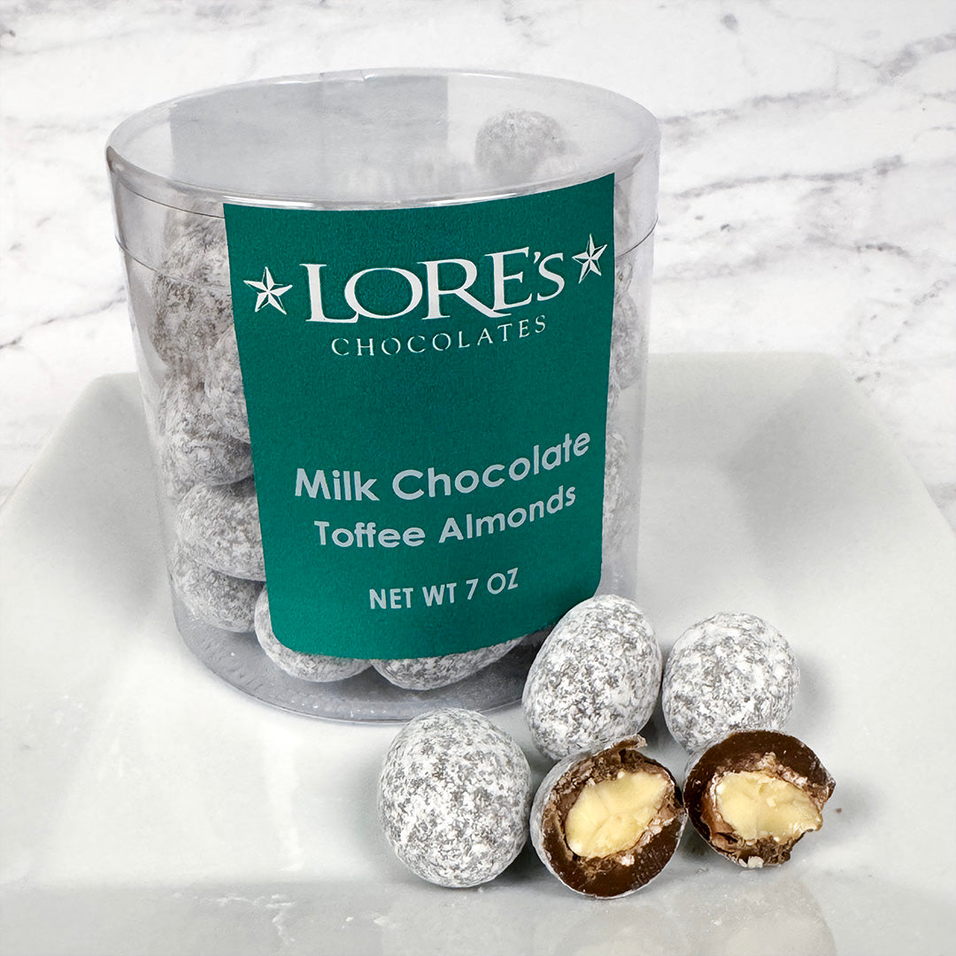 Clear container of milk chocolate toffee almonds with a green label with "Lore's Chocolates" logo on a marble surface
