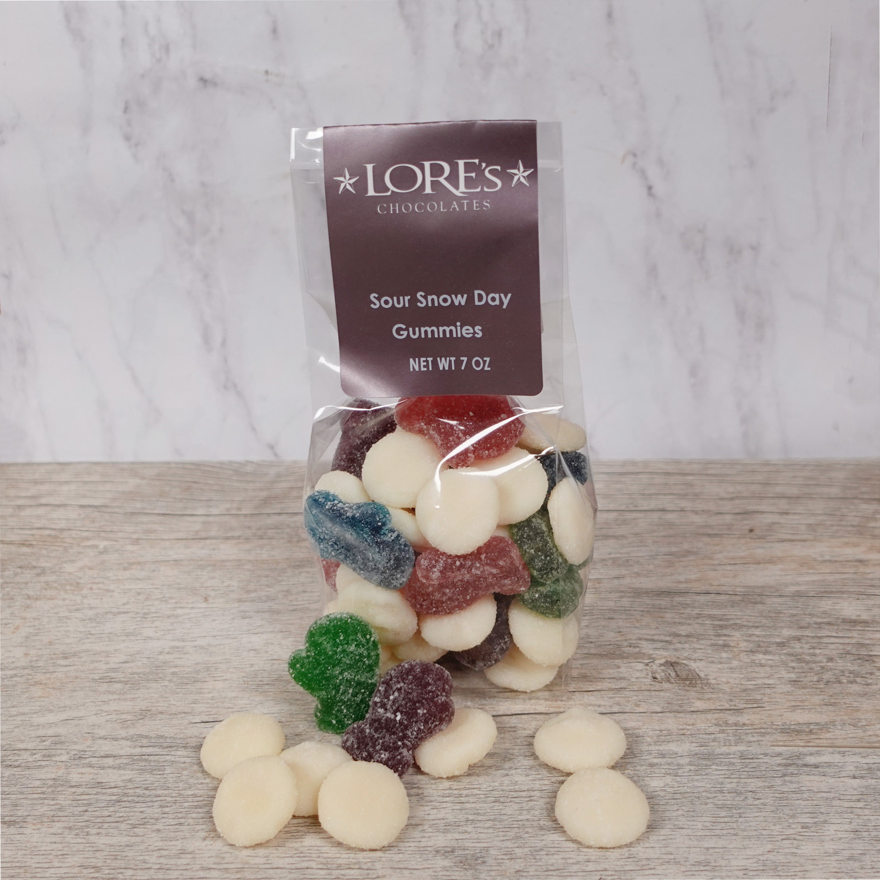Packaged Sour Snow Day Gummies from Lore's Chocolates on a wooden surface with a marble background.
