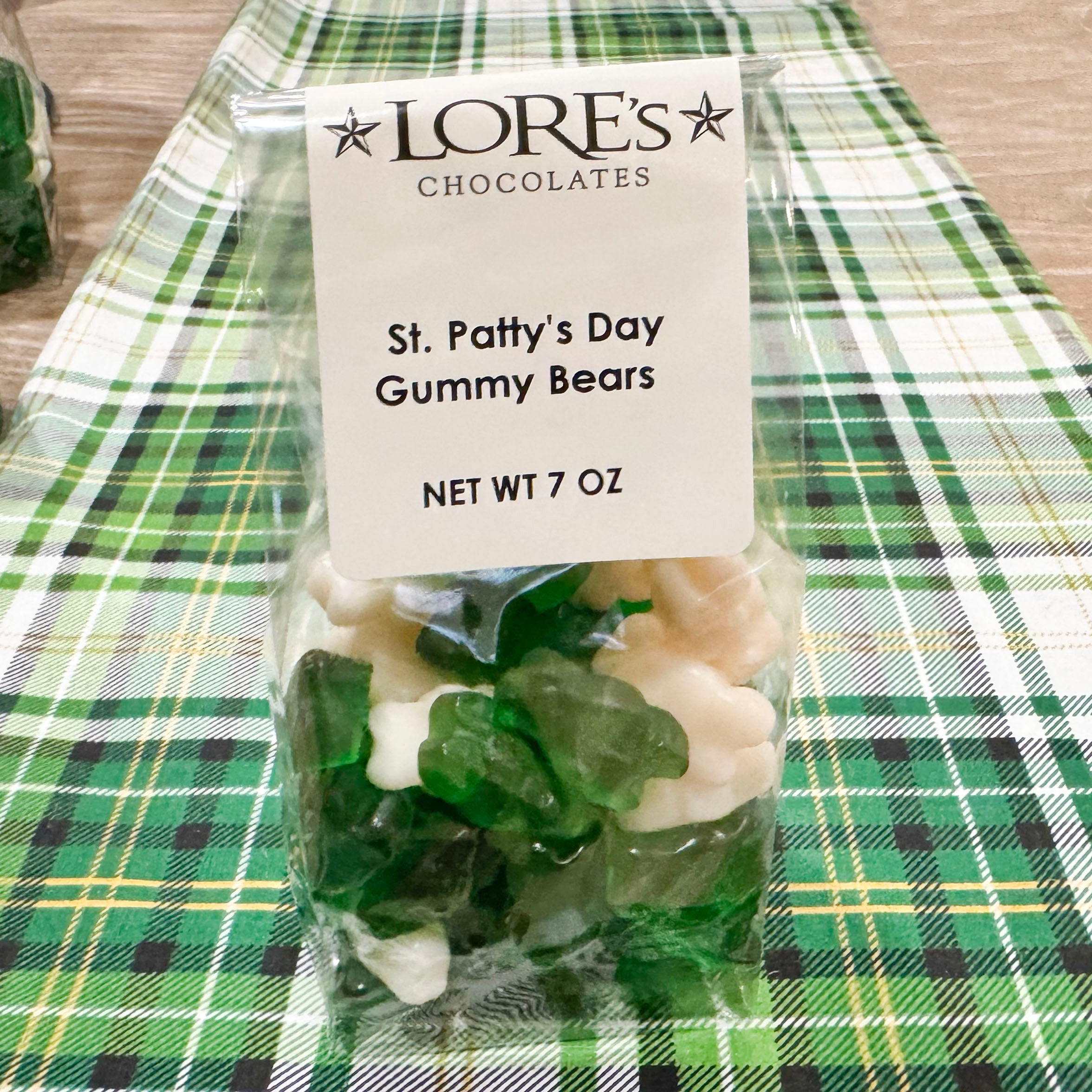 Pack of St. Patrick's Day gummy bears with LORE'S CHOCOLATES packaging on a green plaid tablecloth.