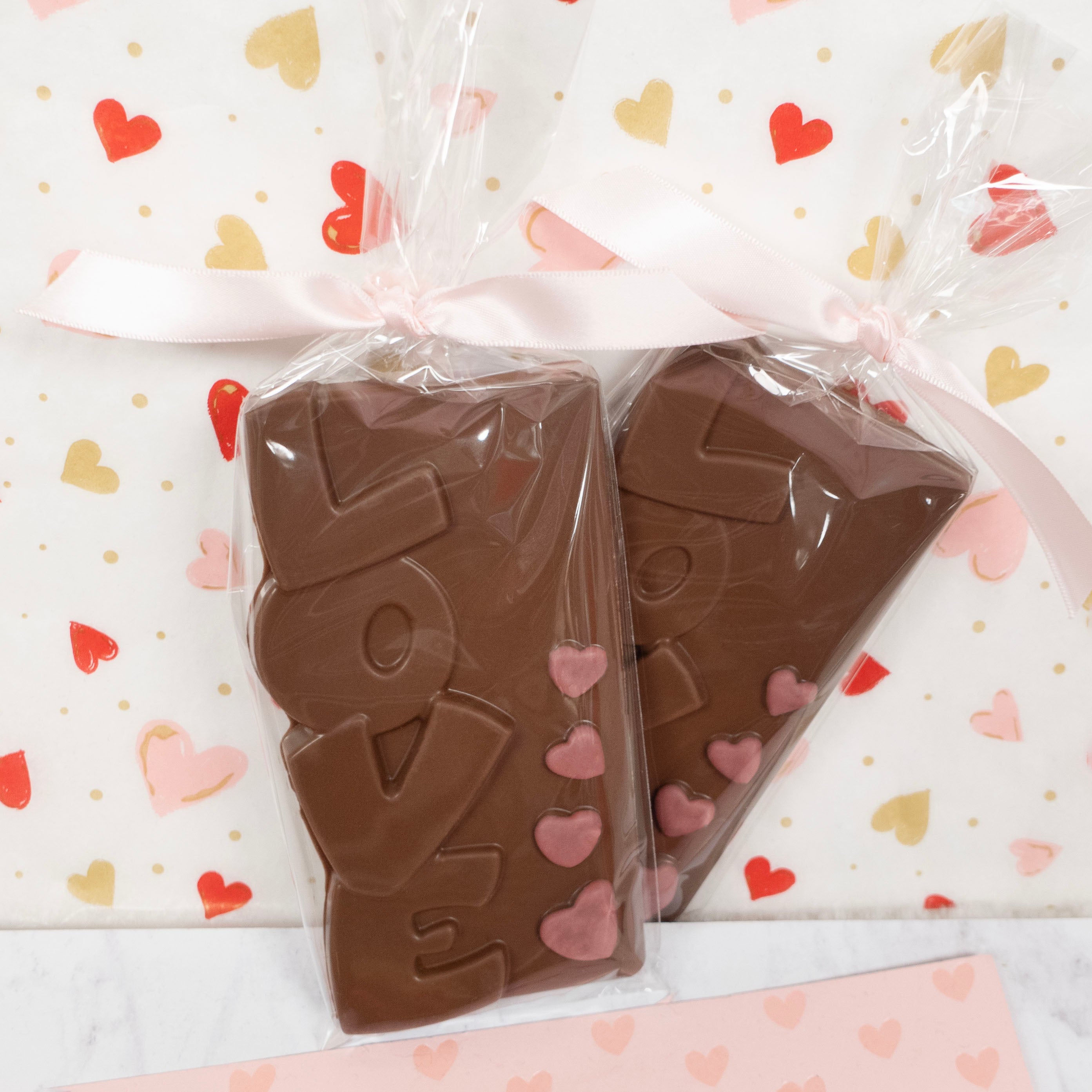 Two pieces of chocolate shaped like the word 'LOVE' on a heart-patterned background.