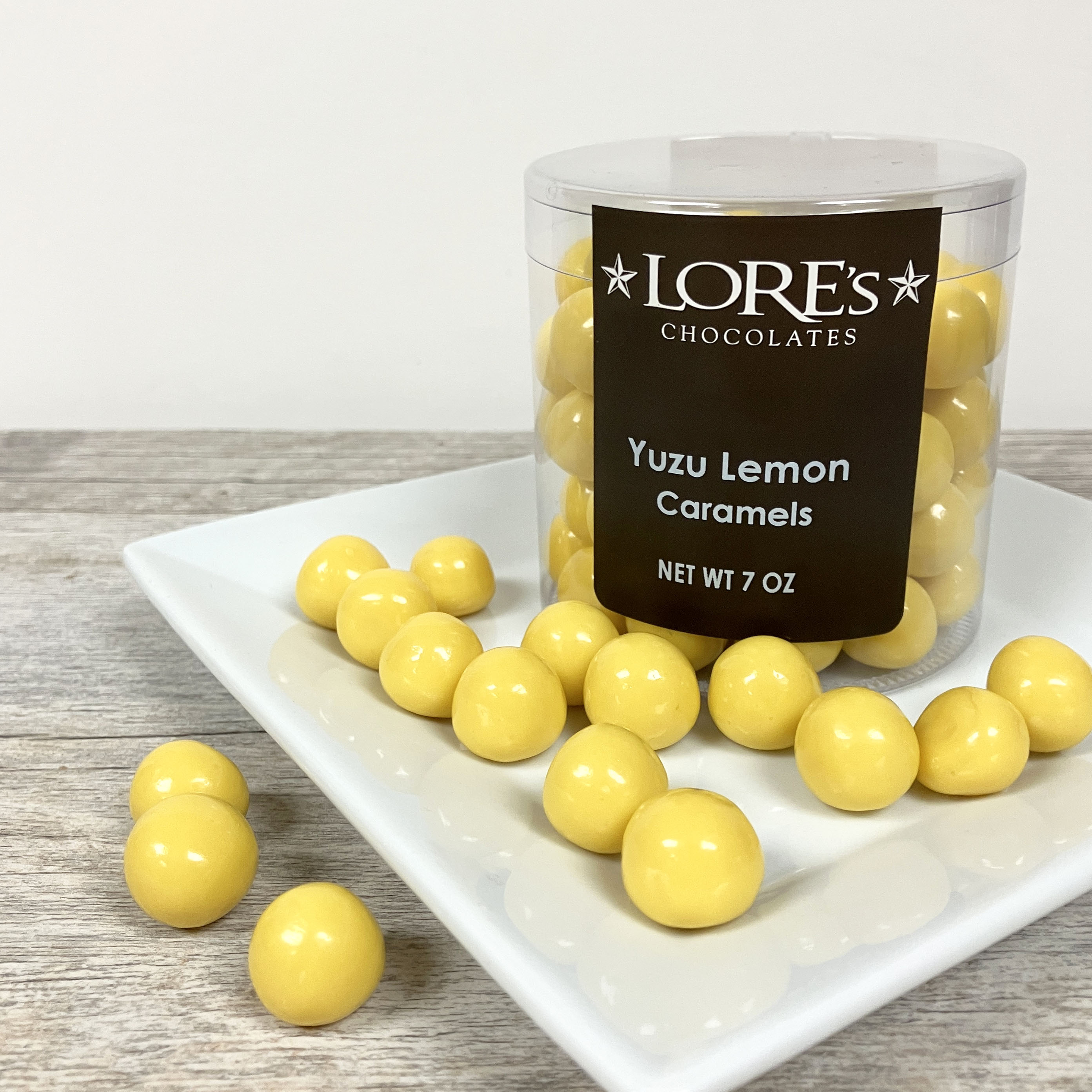 Yellow lemon flavored caramel candies on white square plate - with container reading "Lore's Chocolates, Yuzu Lemon Caramels, Net Wt 7 oz"
