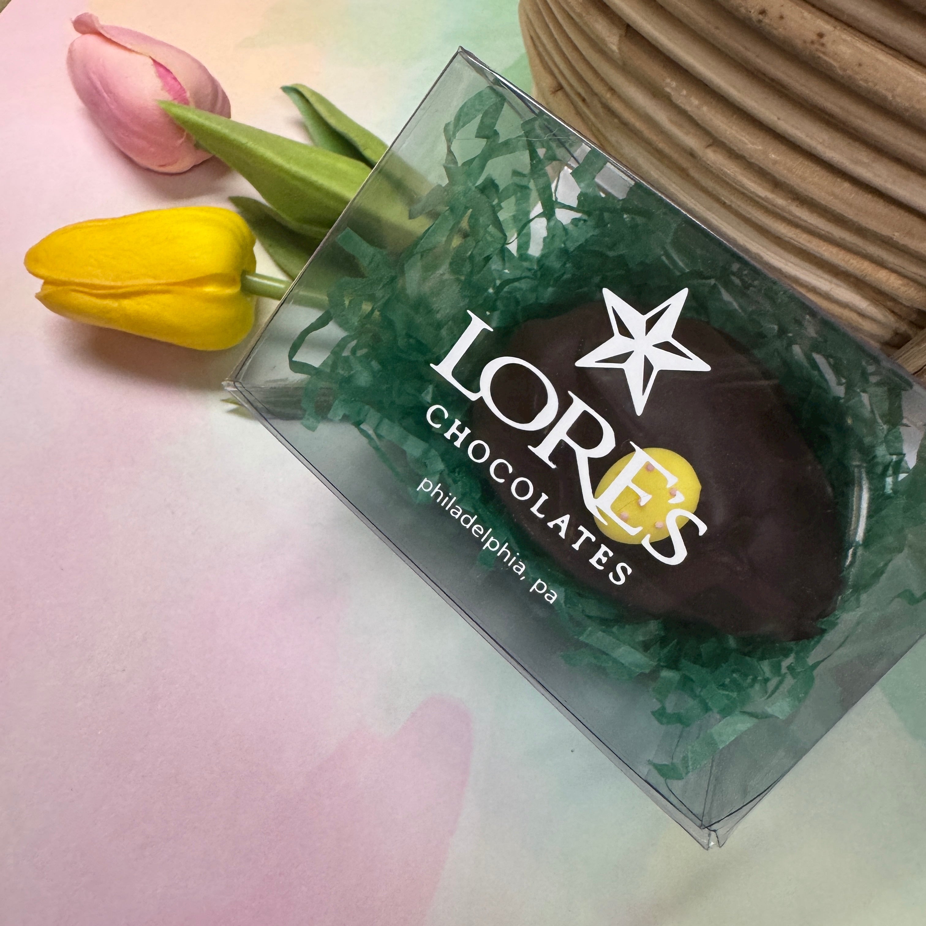 1/4 dark chocolate hand-rolled easter egg with yellow egg sugar decoration in a clear gift box that reads "Lore's Chocolates, philadelphia, pa"