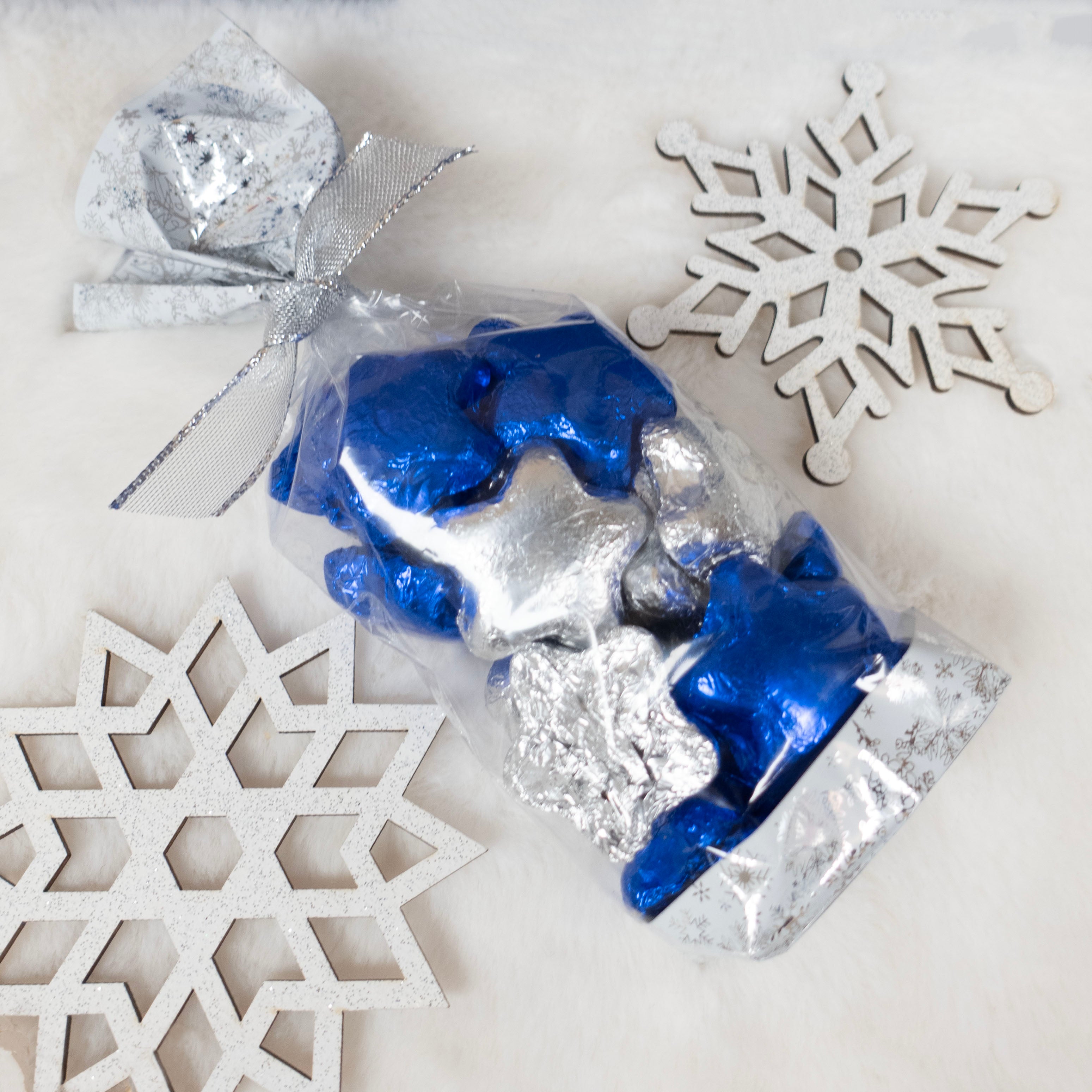 Blue and silver foiled chocolate candies in clear packaging with decorative snowflakes on a light background