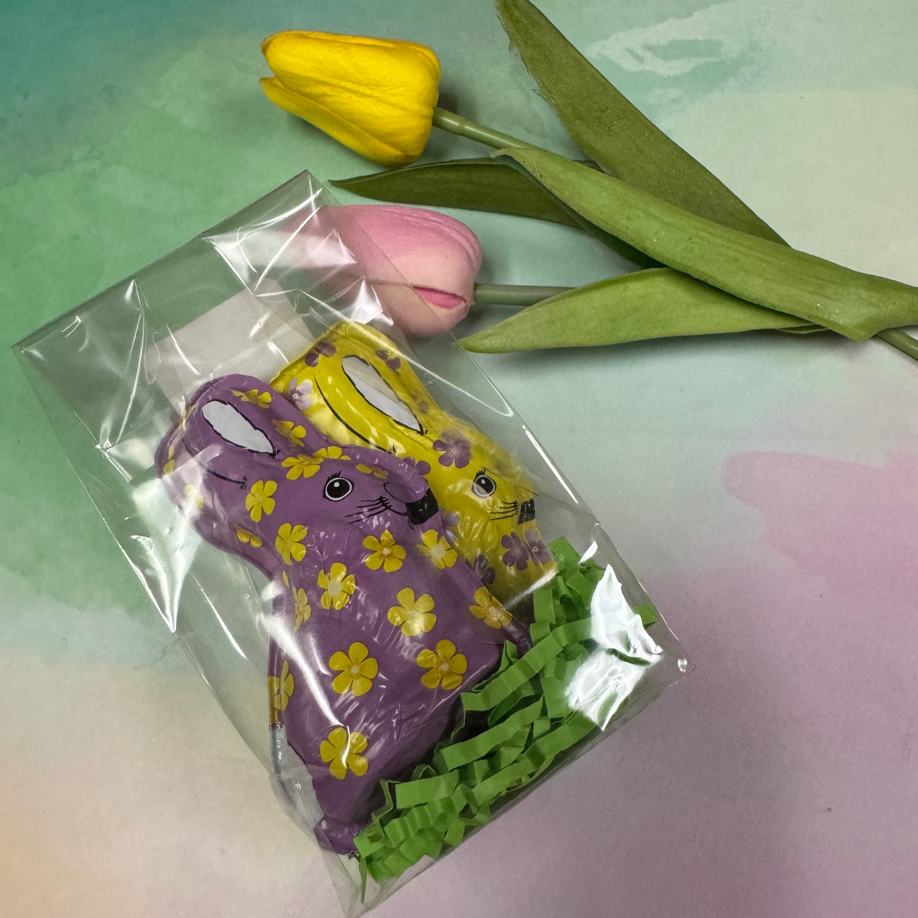 purple foiled bunny with yellow flowers and yellow bunny with purple flowers in packaging - bunnies are milk chocolate