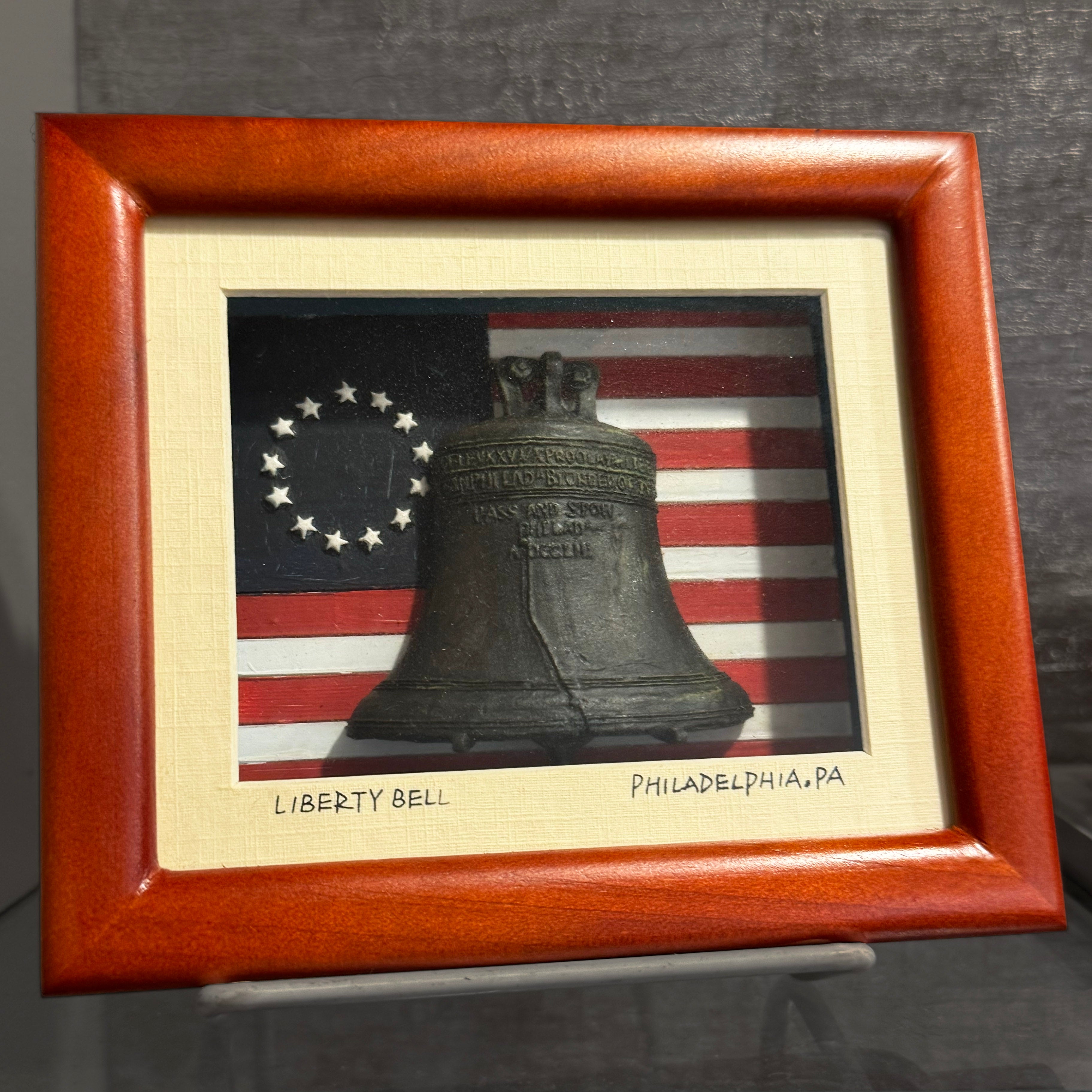 Framed sculpture of the Liberty Bell with a Betsy Ross flag in the background