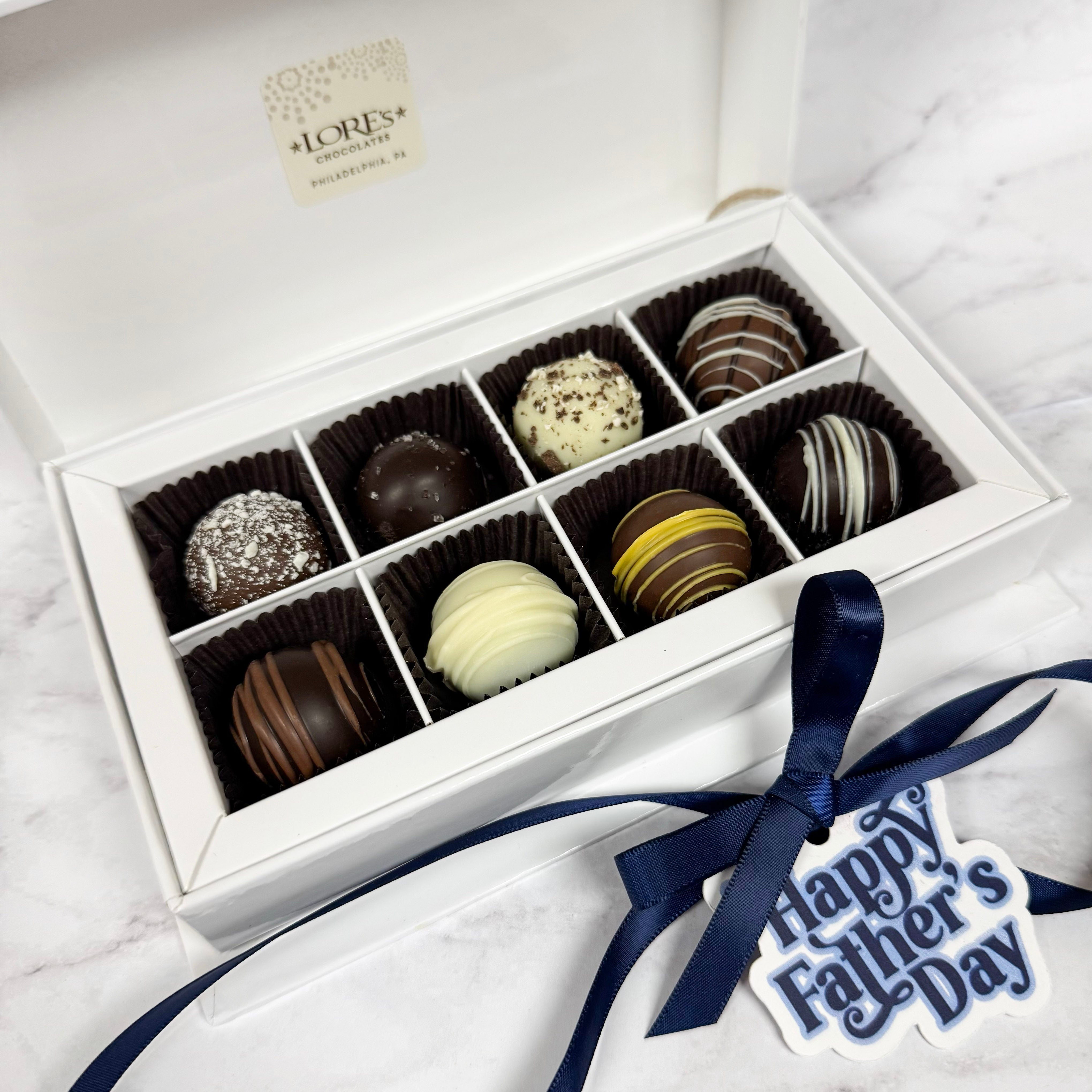 Box of chocolates truffles with a 'Happy Father's Day' hang tag on a white marble surface