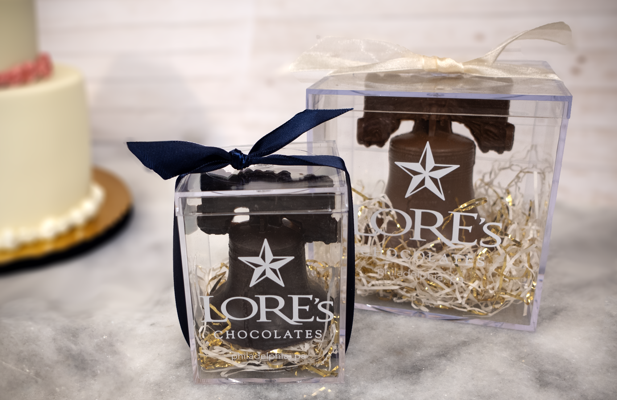 Lore's Chocolates philadelphia pa, chocolate liberty bells in clear hard cases, with a wedding cake out of focus in the background
