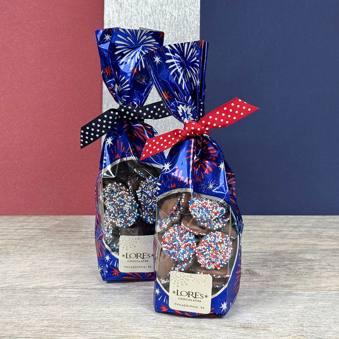 Chocolate nonpareils in decorative patriotic packaging for America 250 with festive designs on a wooden surface. Lore's Chocolates in Philadelphia
