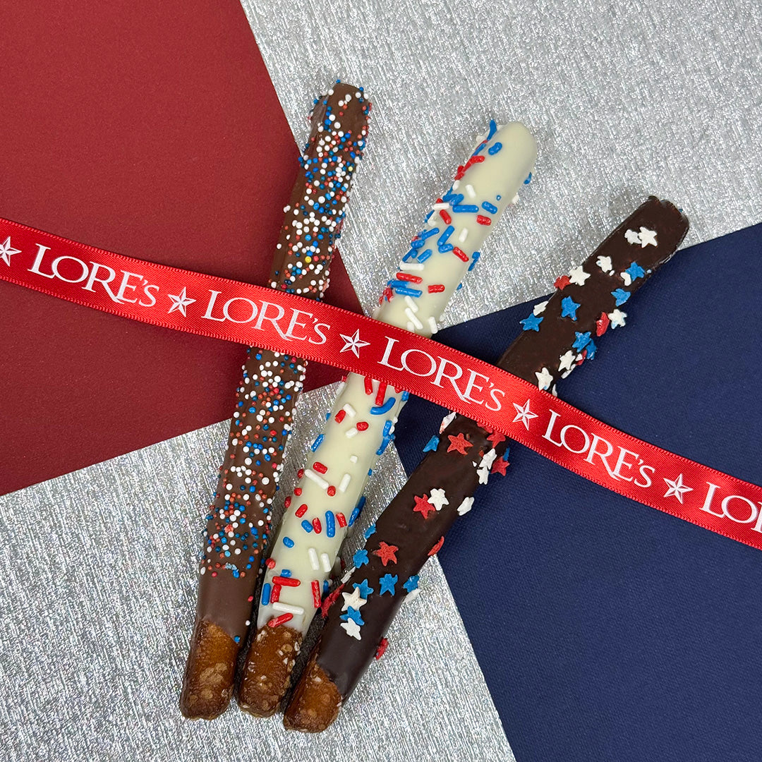 Decorated red, white, and blue, patriotic pretzel rods with colorful sprinkles and a red 'LORES' ribbon on a multicolored background.