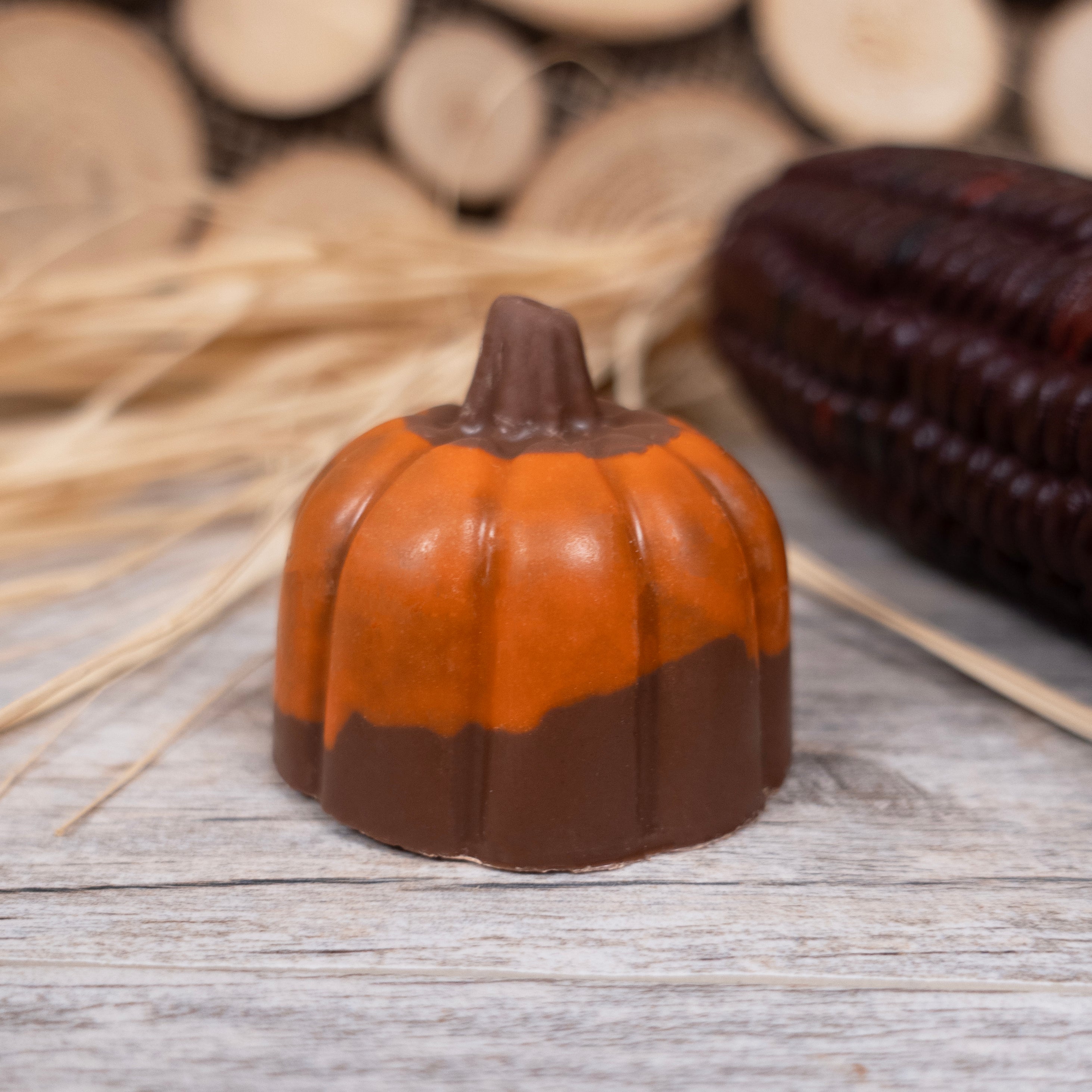 Chocolate pumpkin-shaped candy on a wooden surface with corn and straw in the background