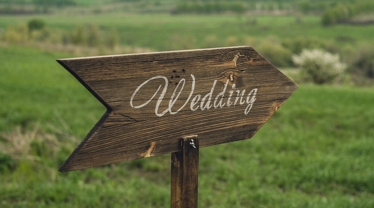 Wooden sign shaped like an arrow pointing right, sign reads "Wedding", green grassy background