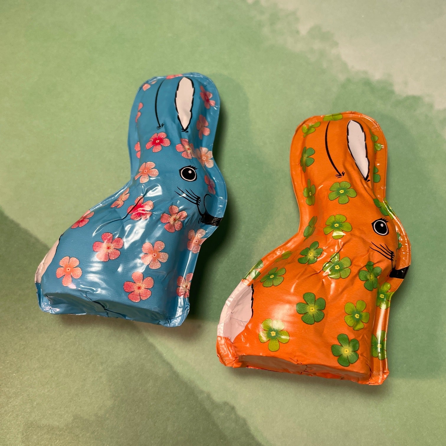 two foiled milk chocolate bunnies, one is blue with pink flowers the other is orange with green flowers.