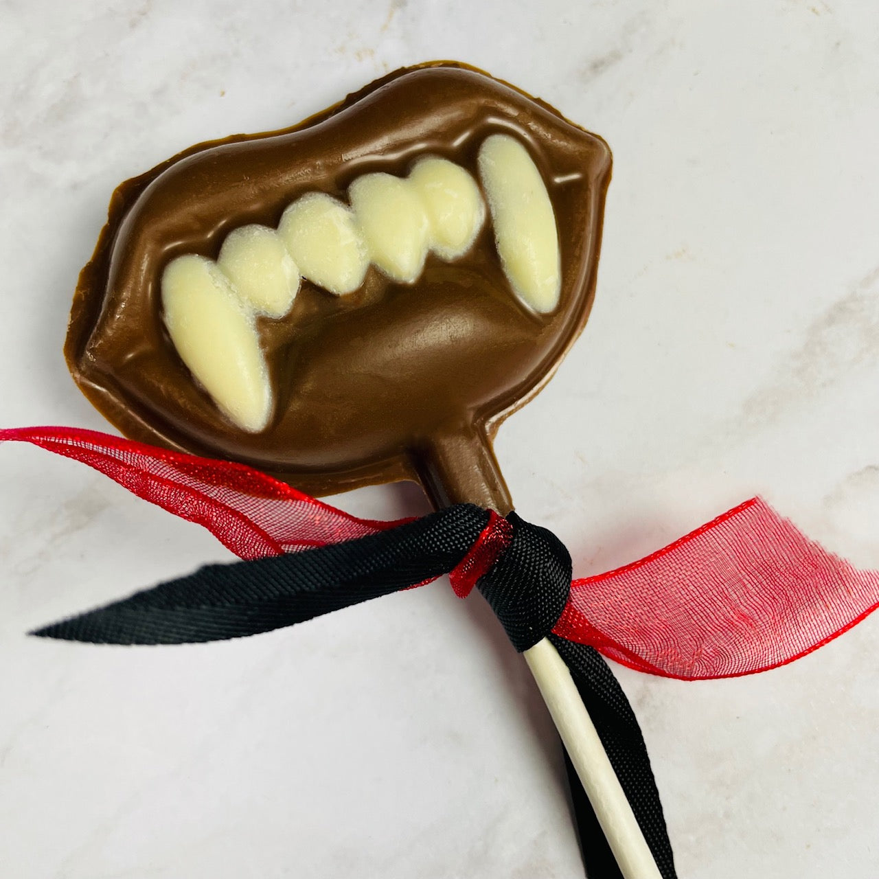 Halloween lollipop shaped like a vampire mouth with fangs. Milk chocolate lips and white chocolate teeth.