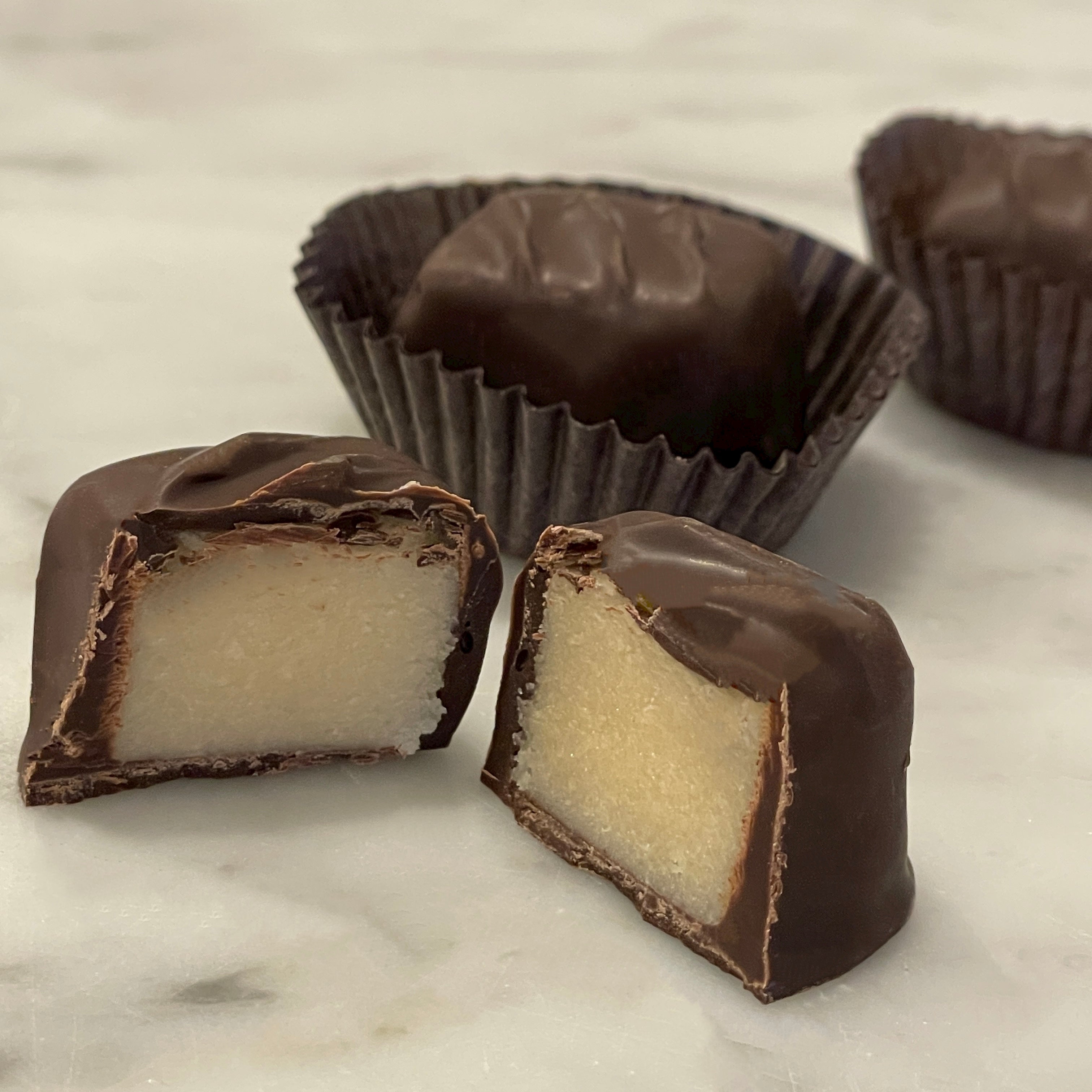 Pieces of dark chocolate marzipan on a marble surface, with one piece cut to show the almond paste inside.