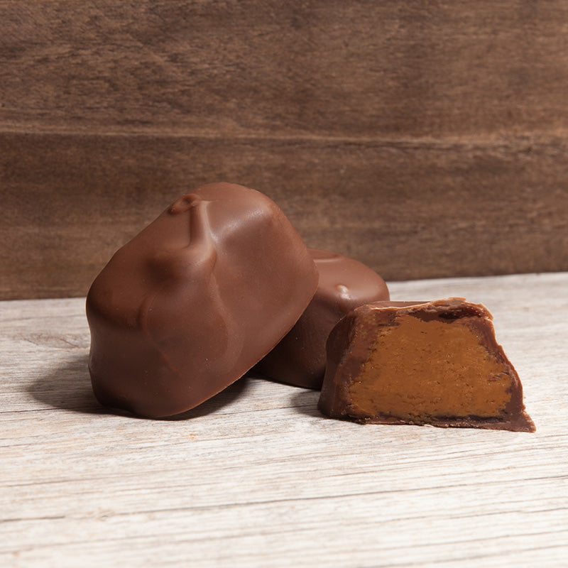 A chocolate-covered peanut butter bite, one cut in half to show the inside, placed on a wooden surface.