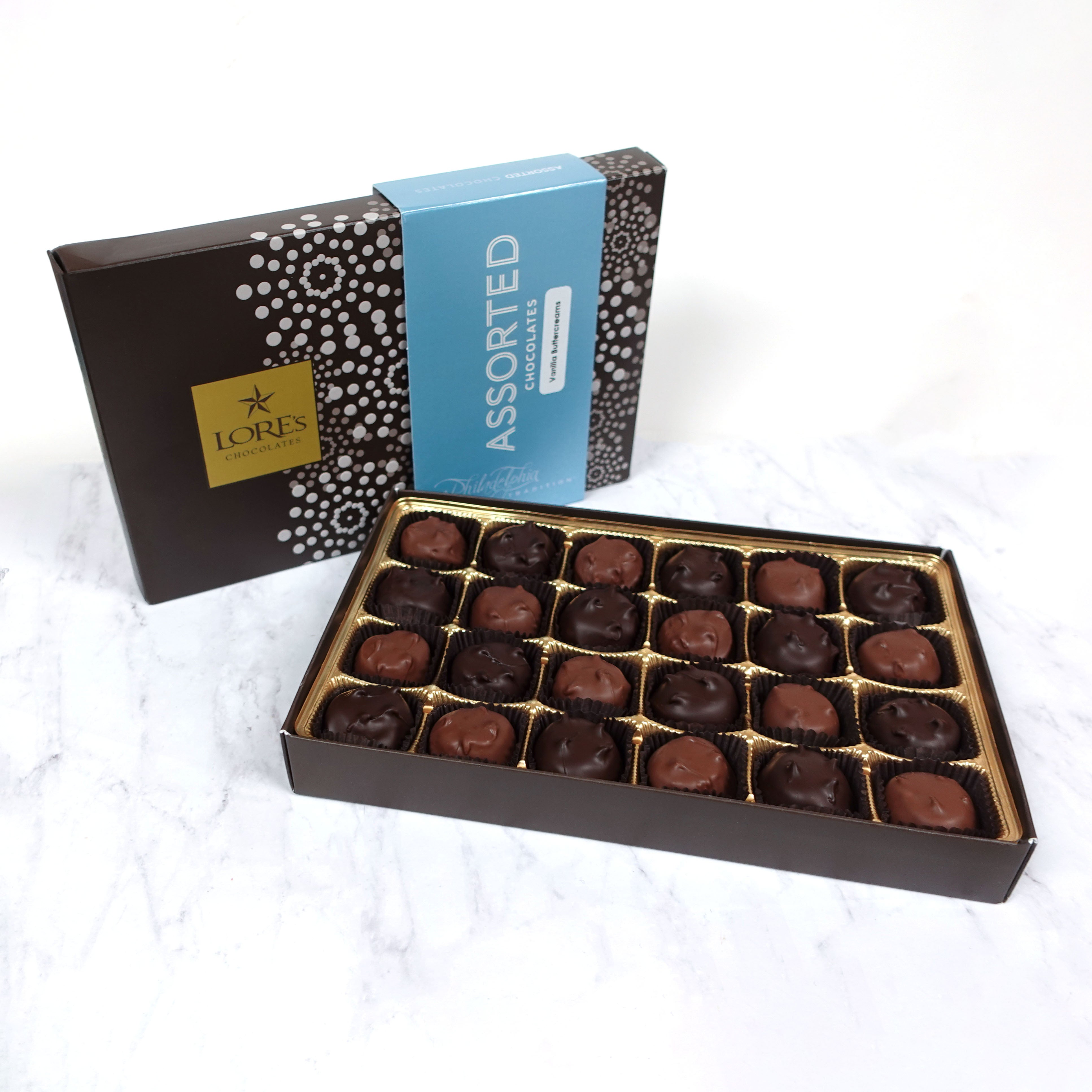 Assorted vanilla butter cream chocolates in an open box with a box labeled 'Lore's' in the background.