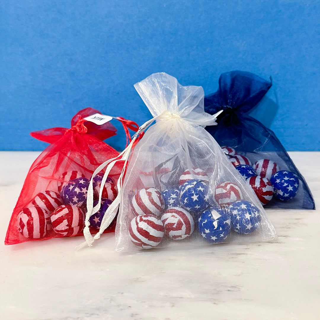 Red, white, and blue star-patterned foiled milk chocolate in see through white, red, and blue bags on a white surface with a blue background.