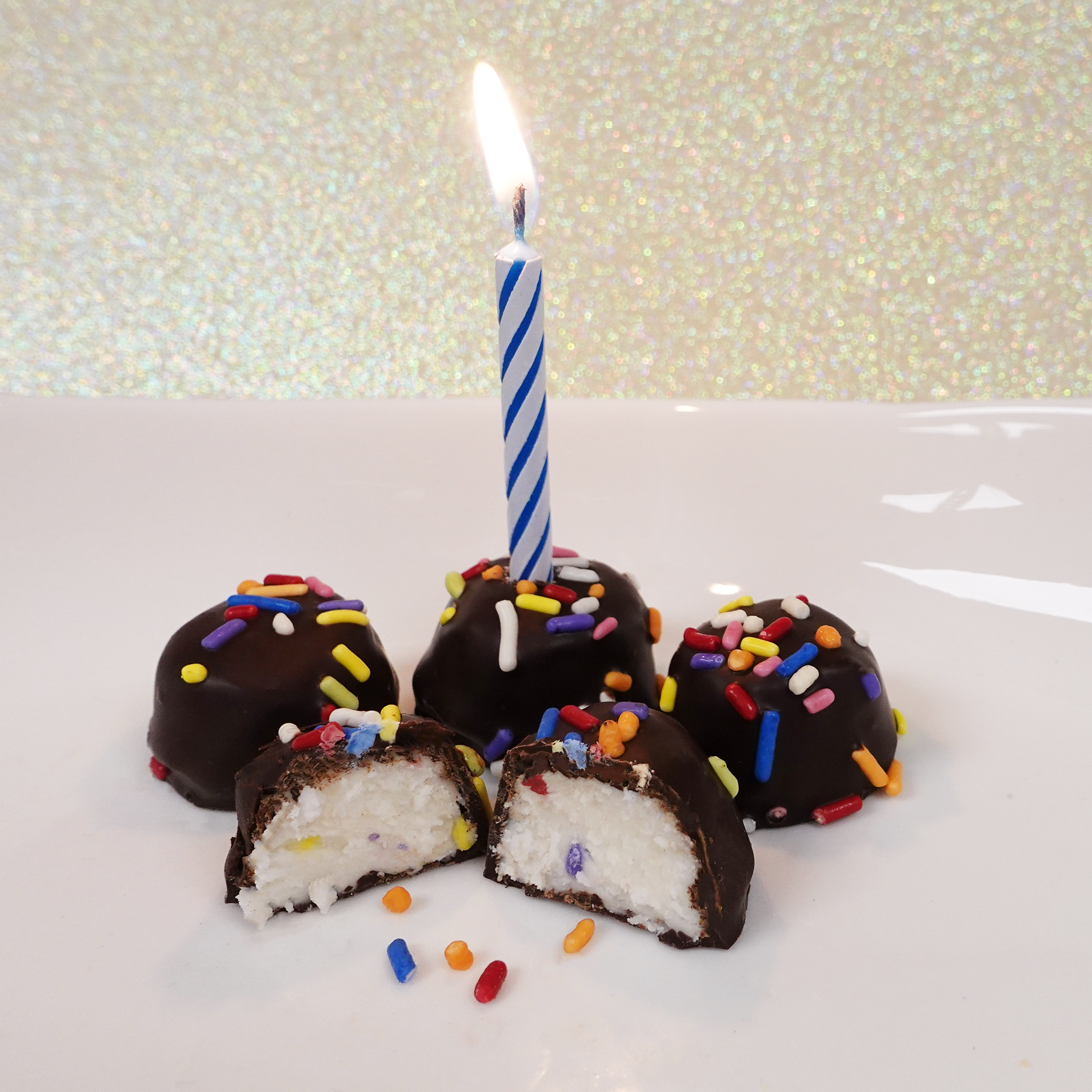 birthday cake butter creams covered in chocolate with rainbow sprinkles. Image shows a birthday candle in one of the chocolates