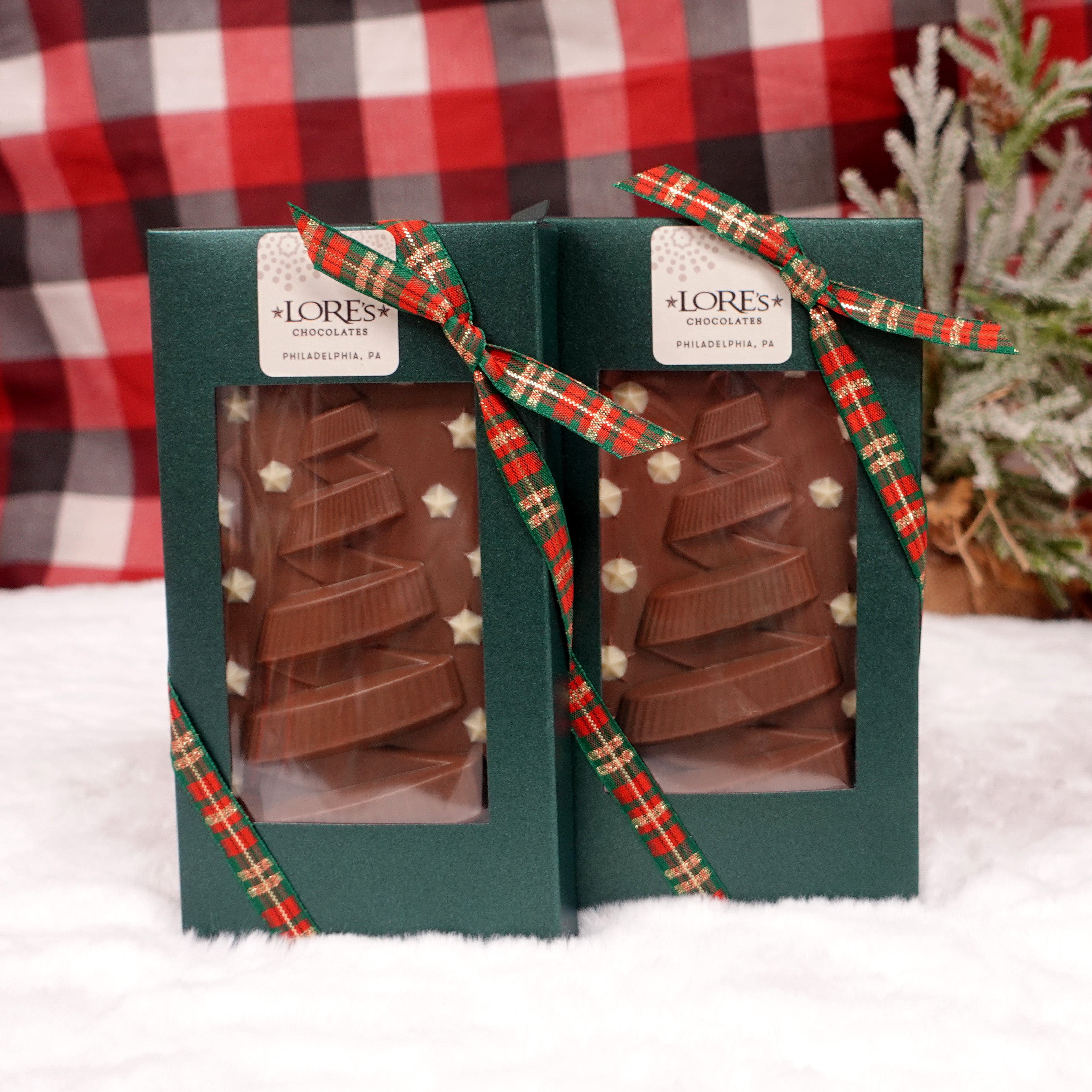 Two milk chocolate bars with ribbon christmas tree designs. packed in a sparkly green box with plaid ribbon