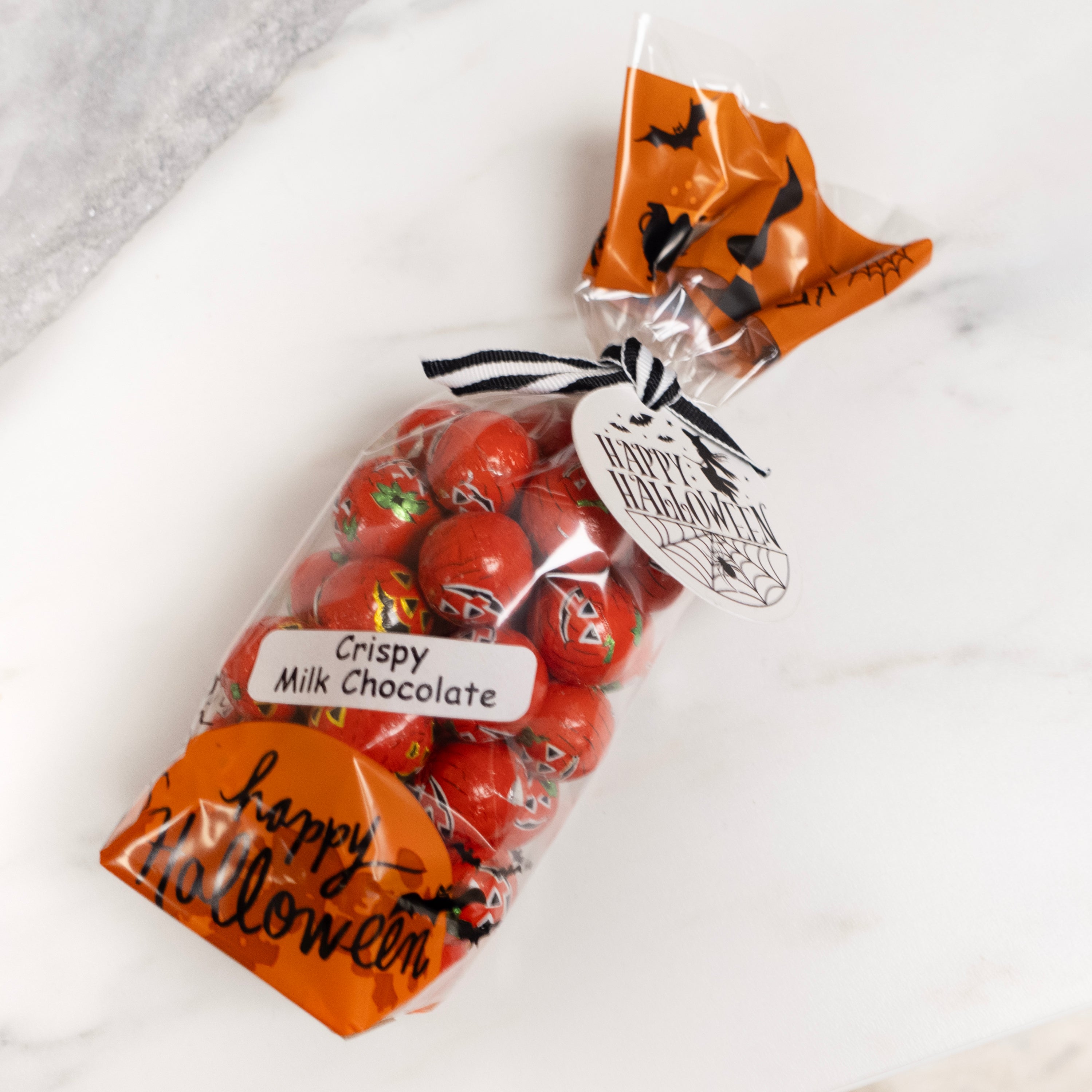 Bag of individually foiled crispy milk chocolate that look like little jack-o-lanterns with Halloween-themed packaging on a white surface