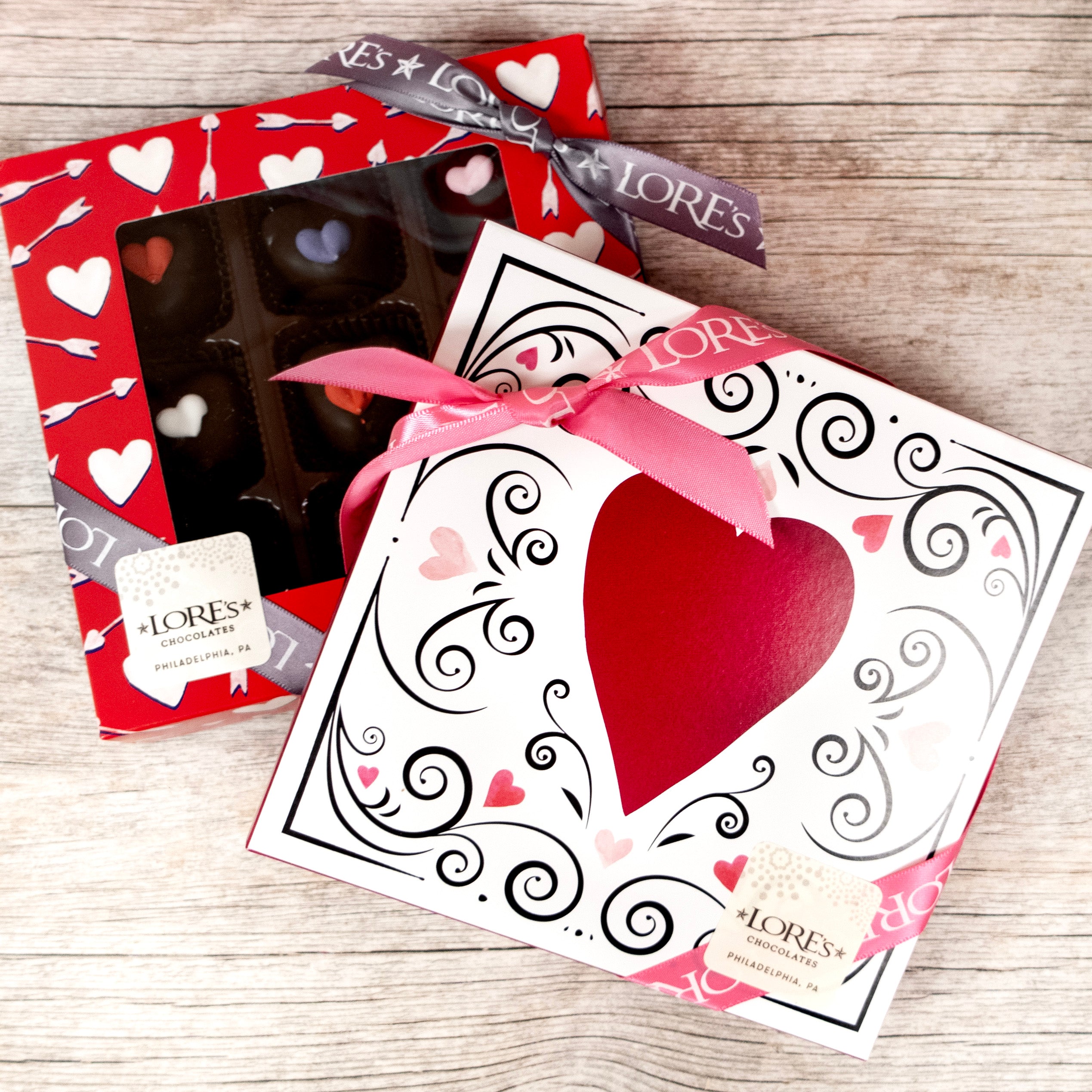 two box designs of valentine's day decorated heart mint cream chocolates - left: hearts and arrows with a red background and a window to see the contents. right: white box with red heart and black swirls