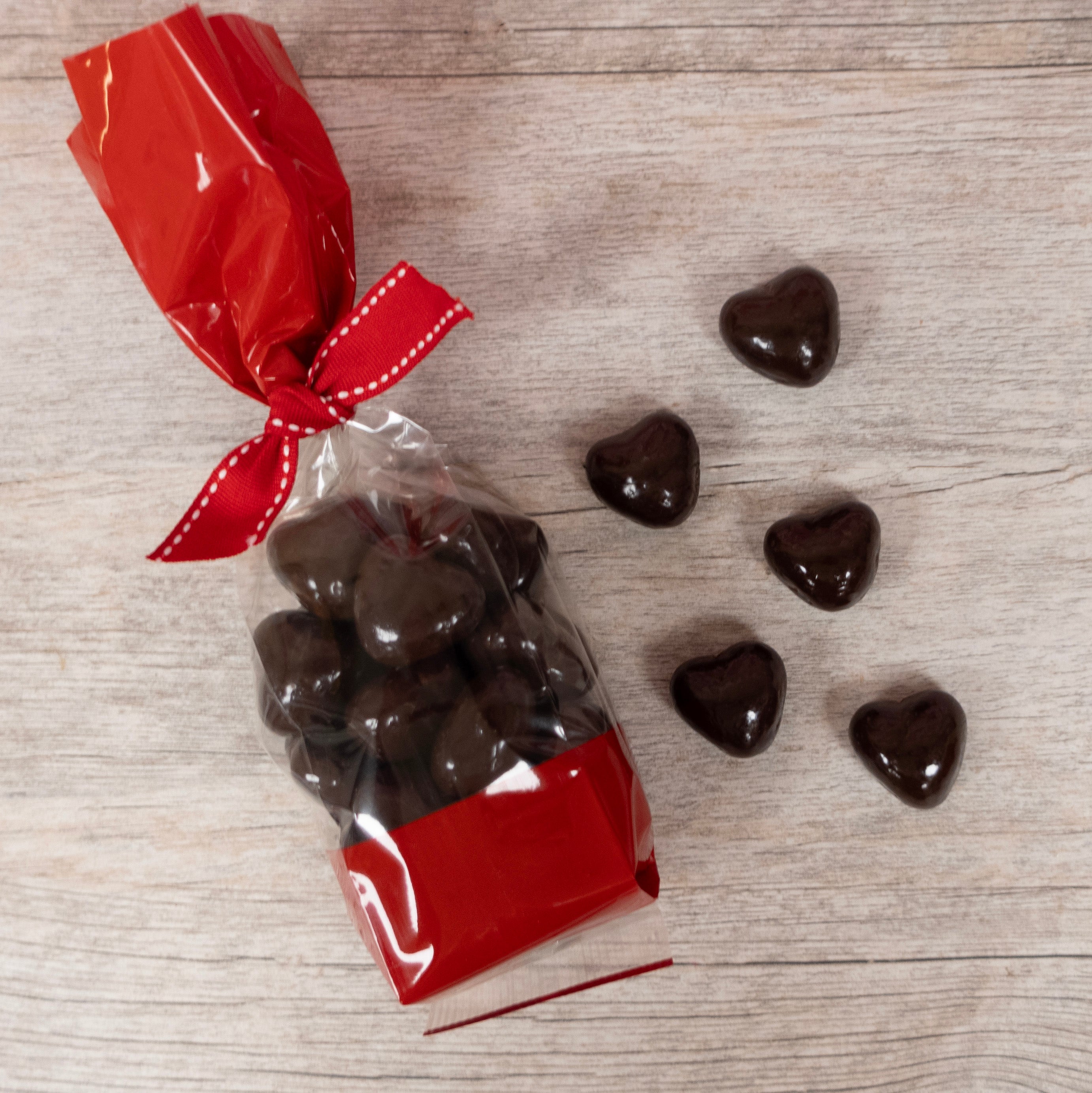 Heart-Shaped Dark chocolate caramels sold by Lore's Chocolates, packaged in a valentine's day cellophane bag with a red ribbon