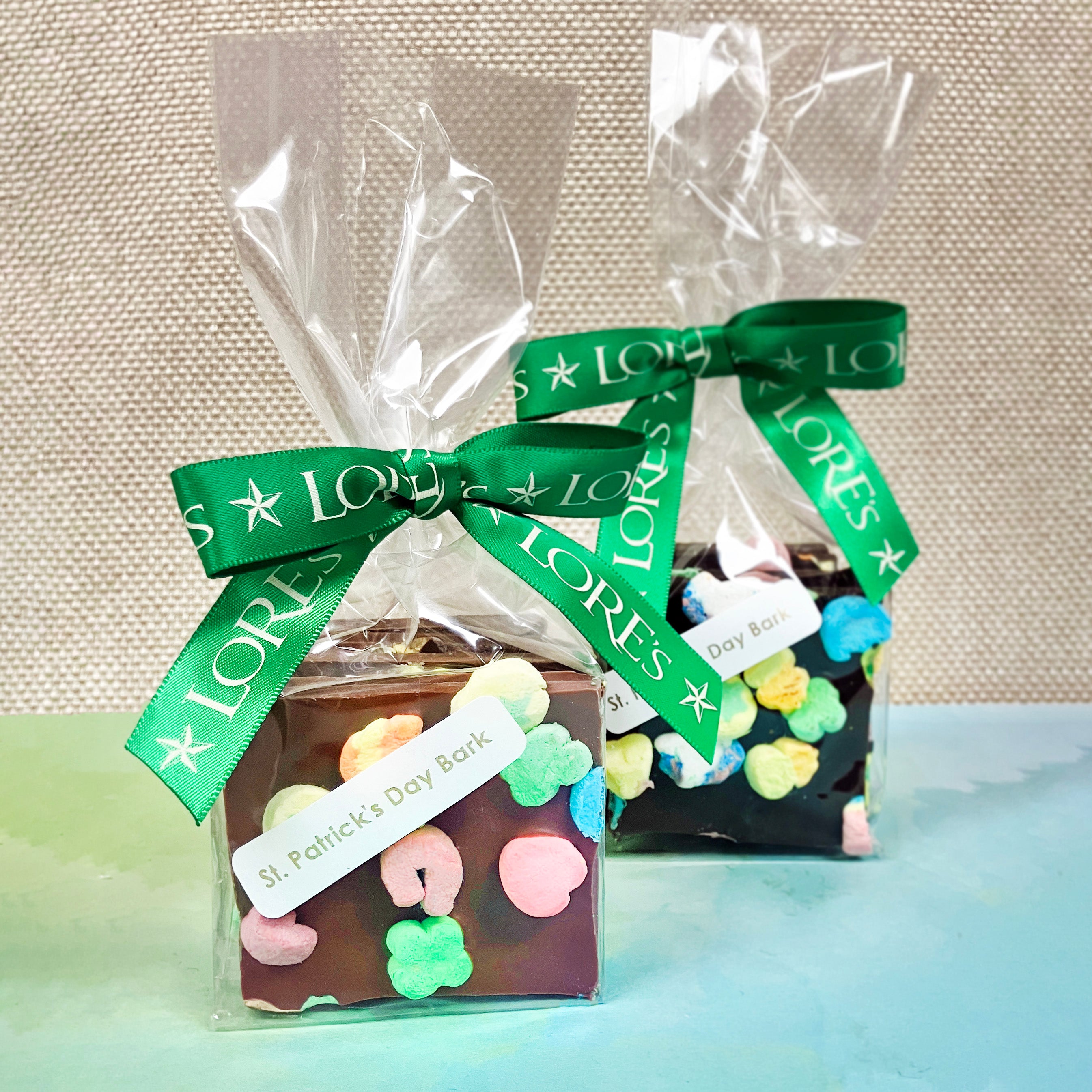 packaged chocolate, milk in front and dark in back all topped with lucky charm's marshmallows. label reads "st patrick's day bark" green ribbon reads "lore's"