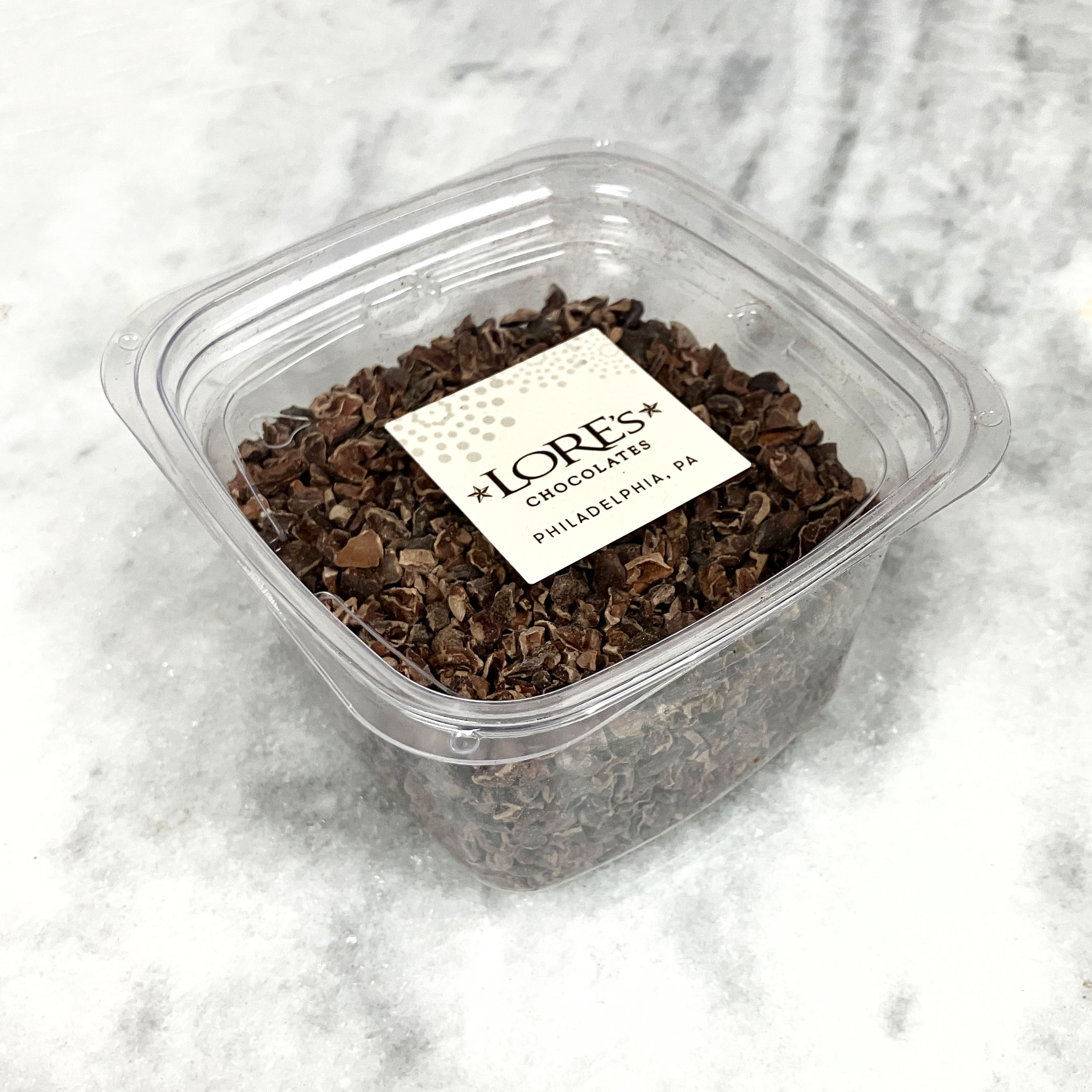 Container of chocolate cacao nibs with a LORES Chocolates label on a marble surface