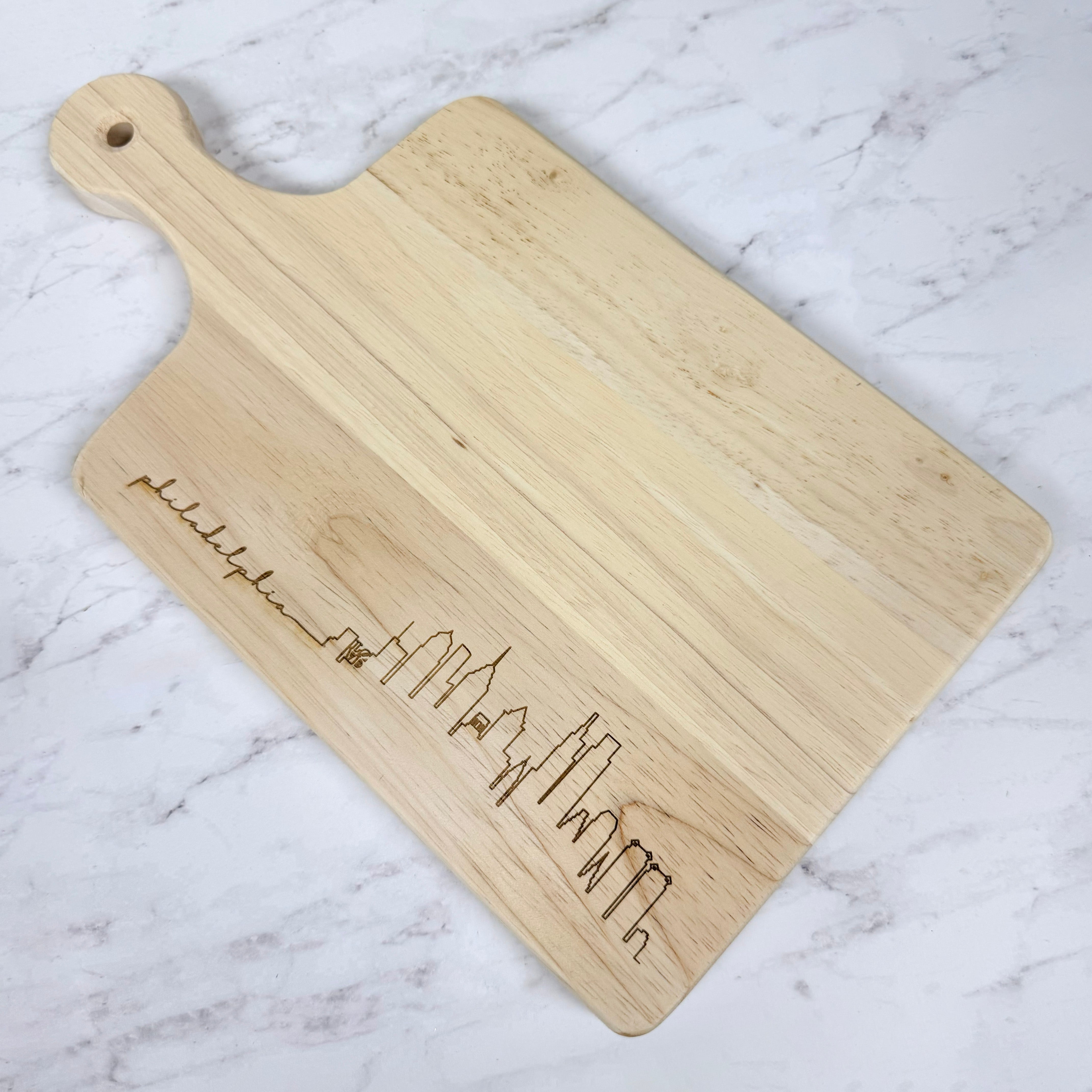 Wooden cutting board with engraved Philadelphia skyline design on a marble surface