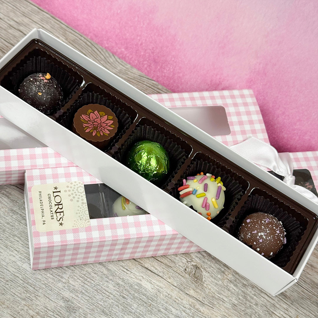Box of assorted chocolate truffles on a wooden surface, packed with a pink checkered gift box. Sold at Lore's Chocolates in Philadelphia