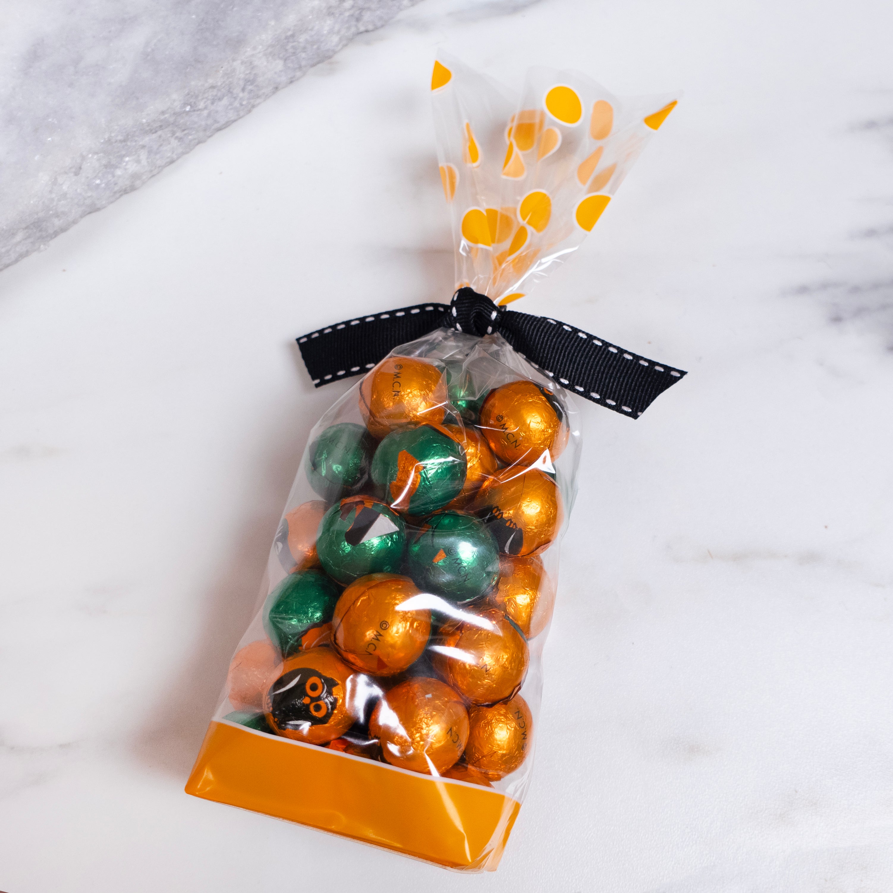 Bag of foiled chocolates with green and orange halloween candies with a decorative ribbon on a marble surface