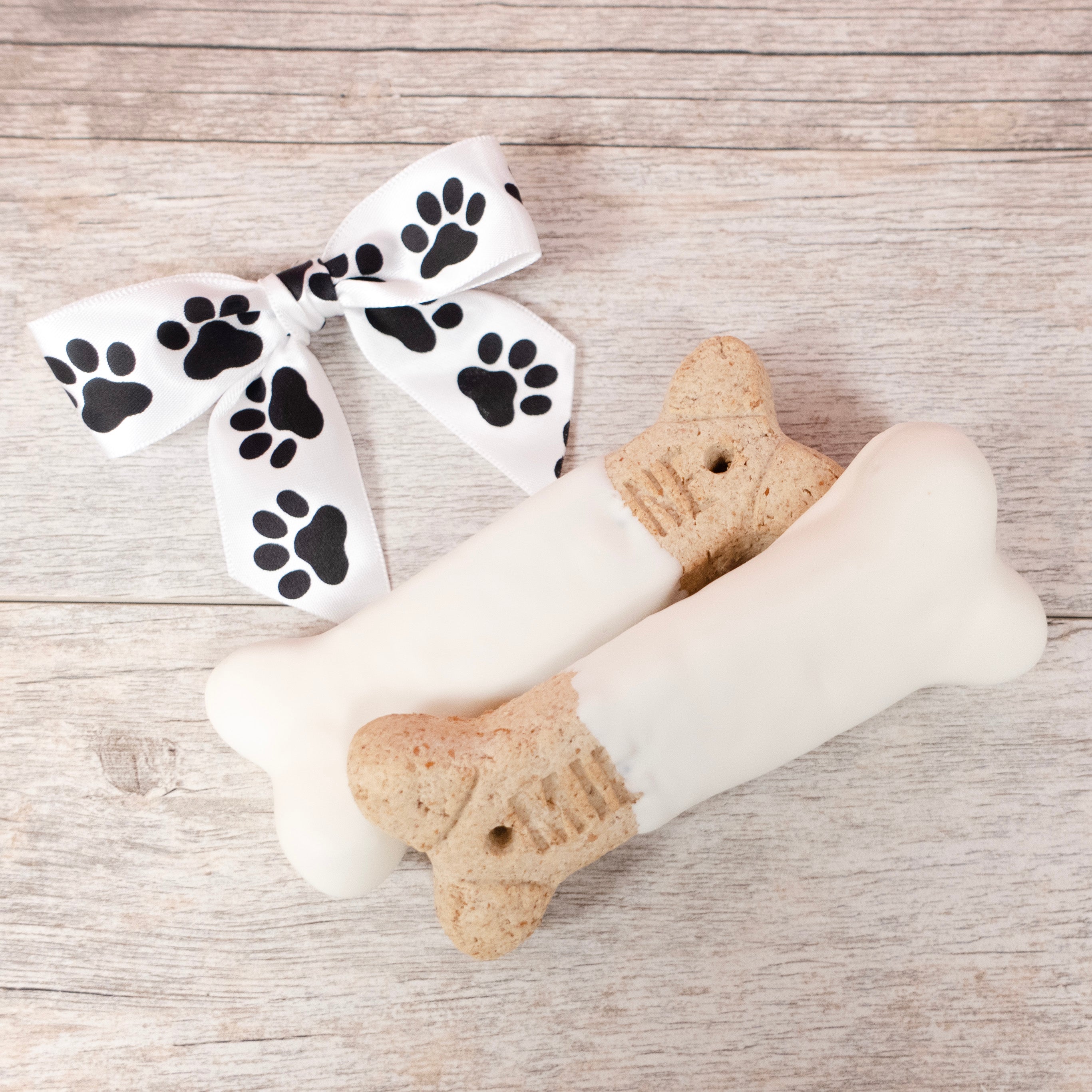 Two Milk Bone Dog biscuits dipped in Lore's Chocolates (dog safe) white yogurt - bow with paw prints in top left corner