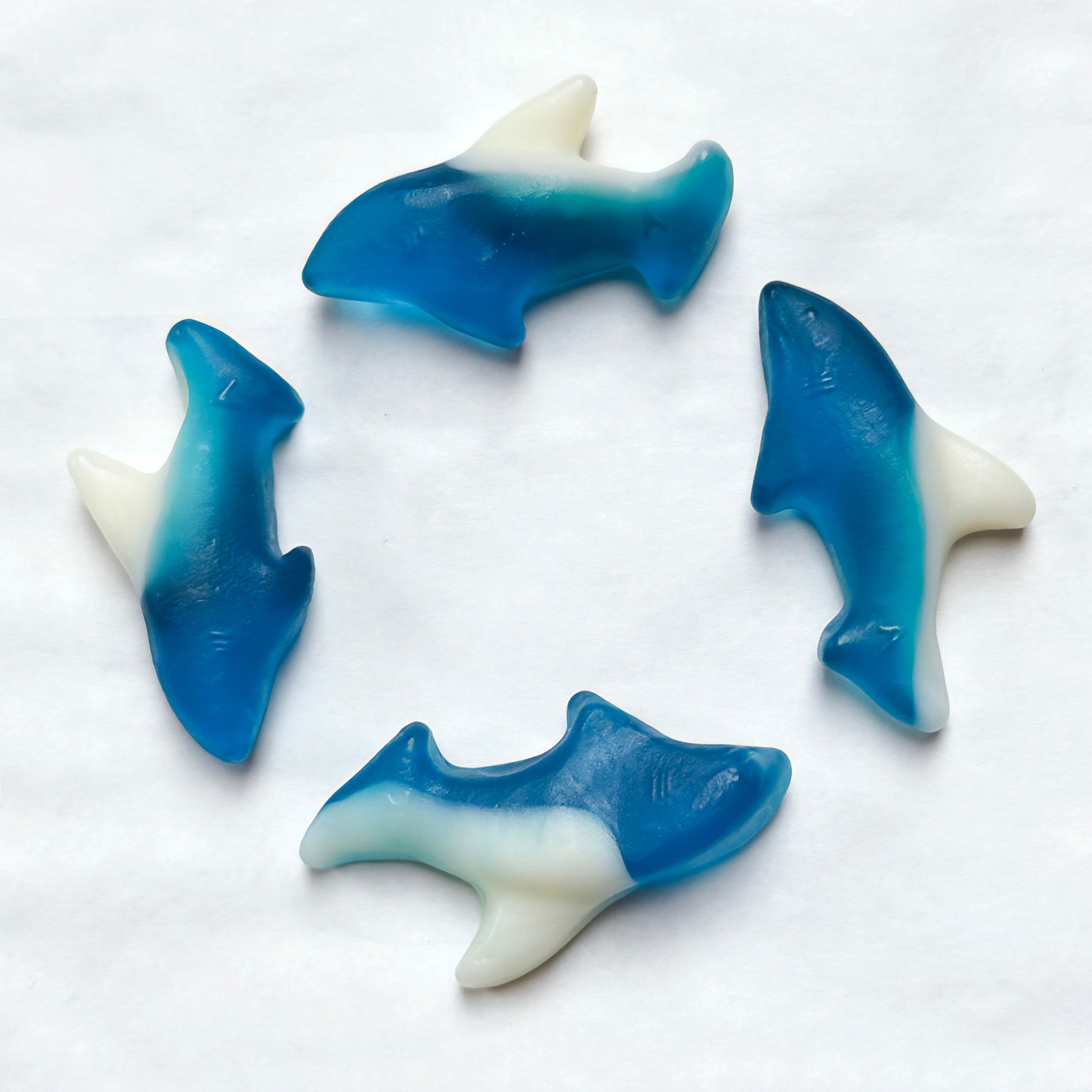 Four blue and white shark-shaped gummy candies on a white background