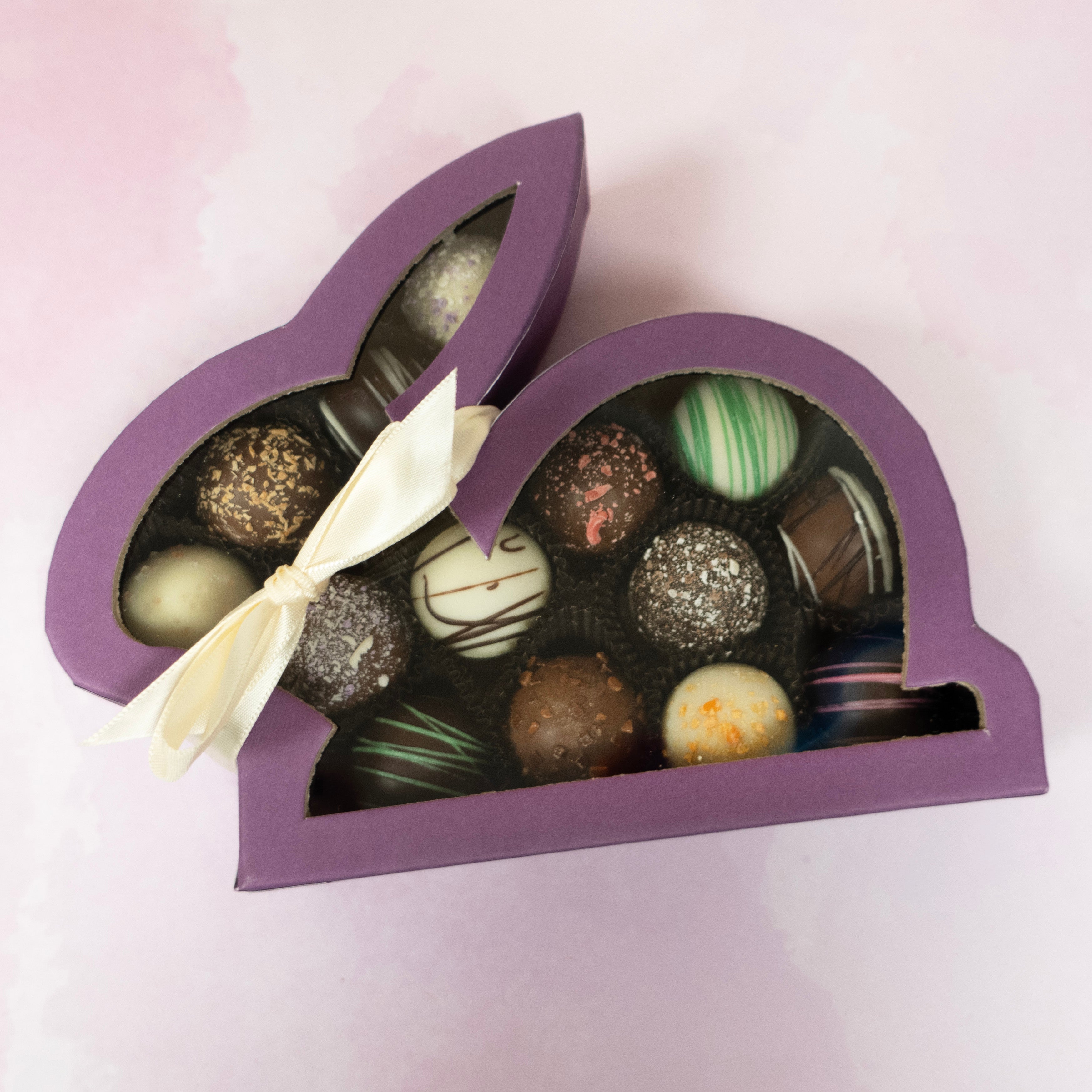 purple window box in the shape of a bunny rabbit full of assorted artisan truffles with a cream colored bow around it's neck