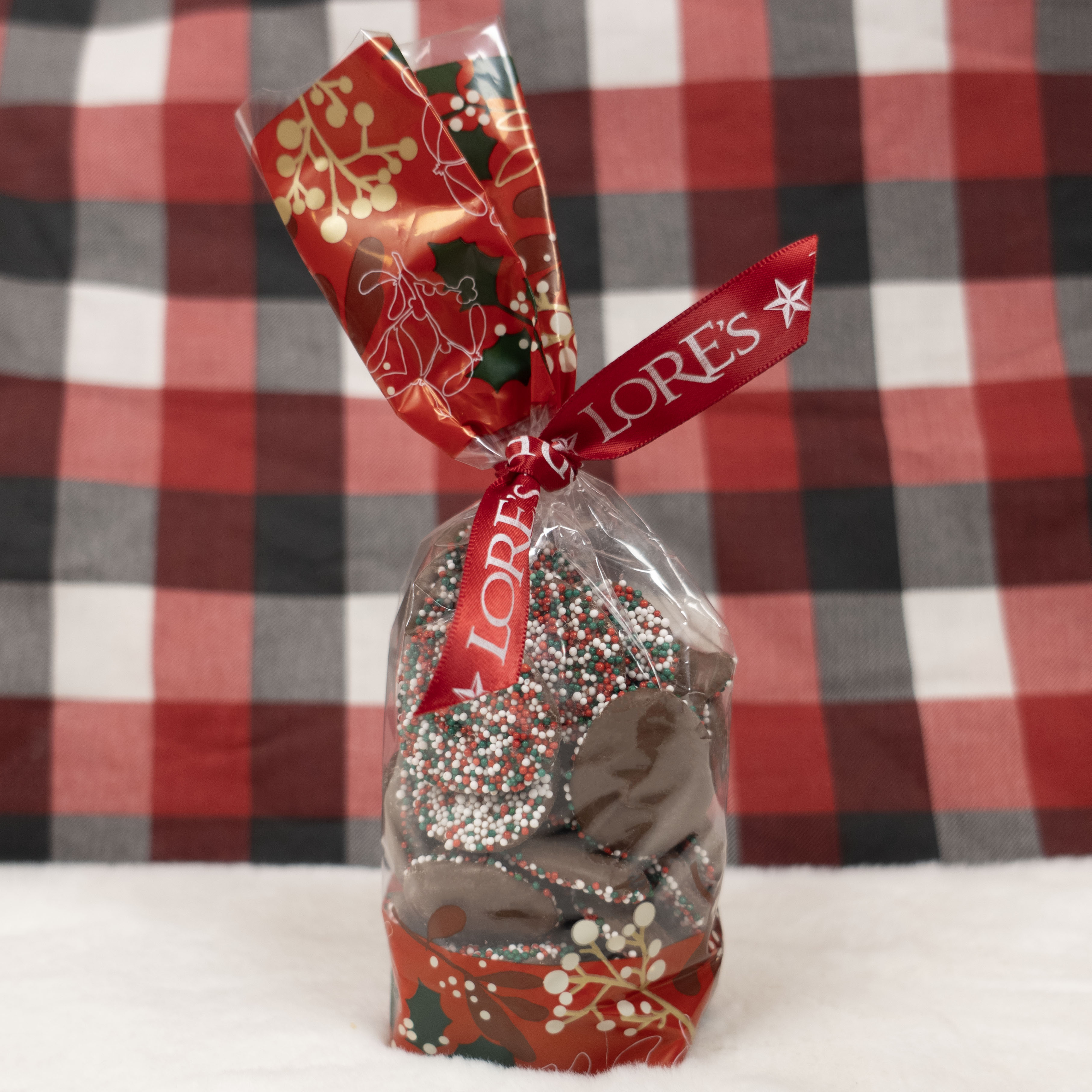 Decorative christmas nonpareil chocolates in a festive bag and a red lore's chocolates ribon against a checkered background