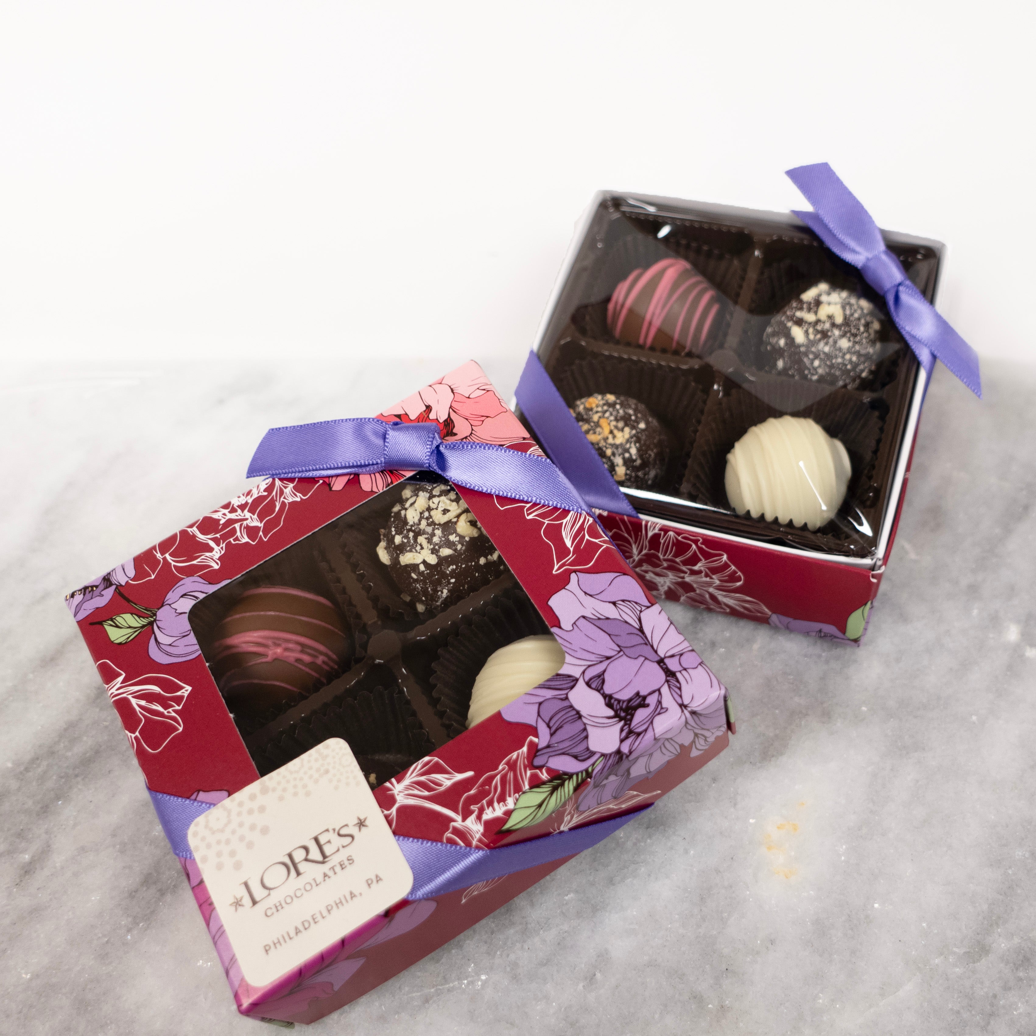 four piece gift box with a clear window to see the 4 piece truffle assortment inside. design is a dark magenta with purple and white flowers, sticker reads lore's chocolates philadelphia pa
