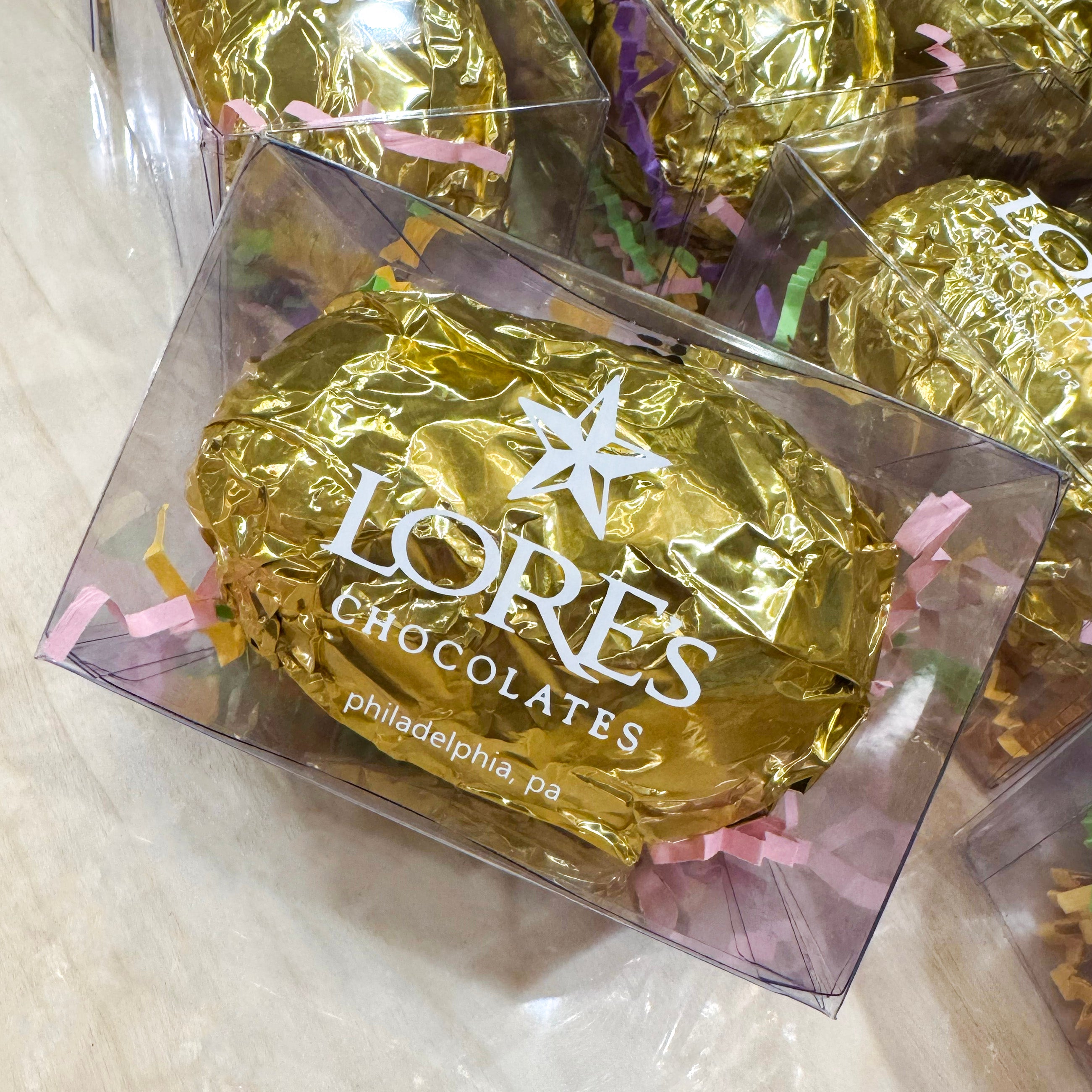 close up of lore's chocolates surprise easter egg in milk chocolate. the egg is foiled with gold and in a clear box