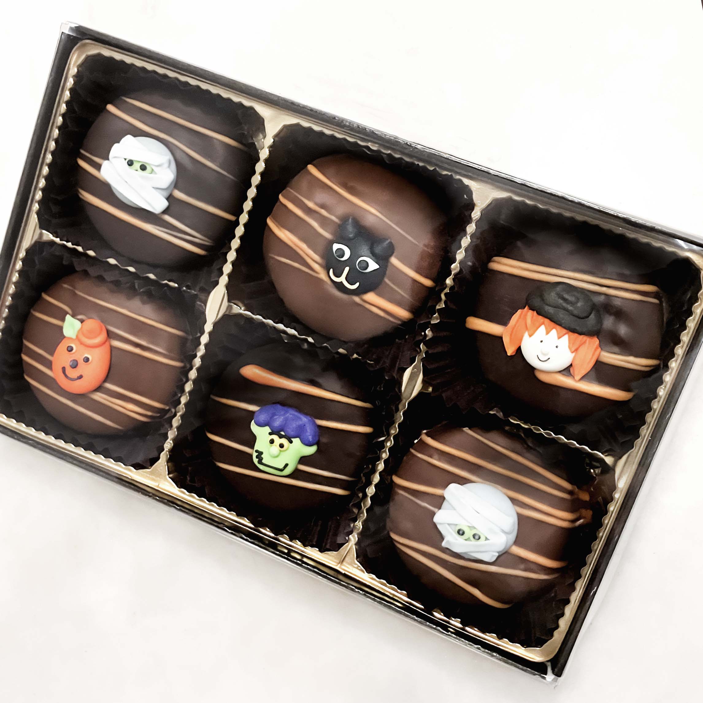 Box of Halloween-themed chocolate oreos with decorative faces on a white background