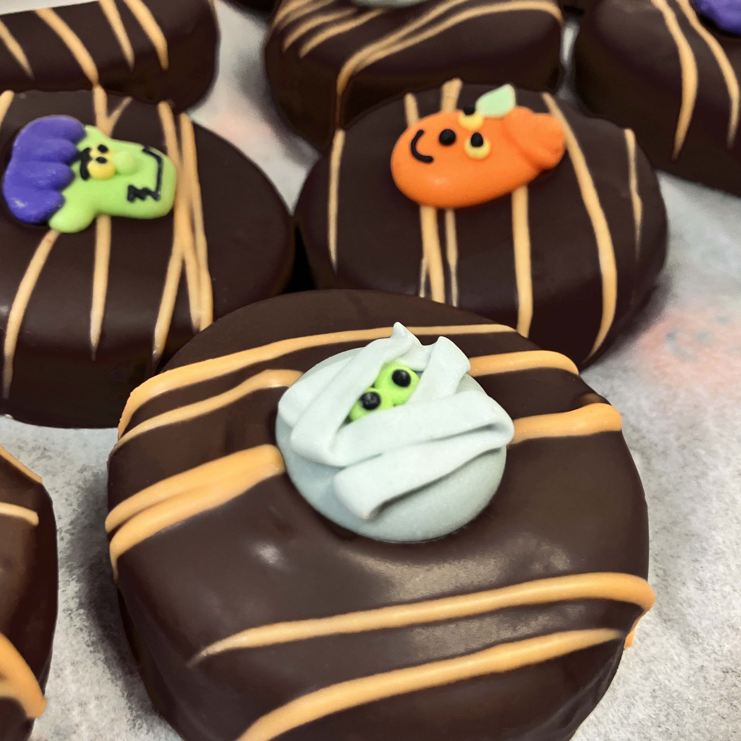 Halloween-themed oreo cookies covered with dark chocolate and decorative elements on a gray surface.