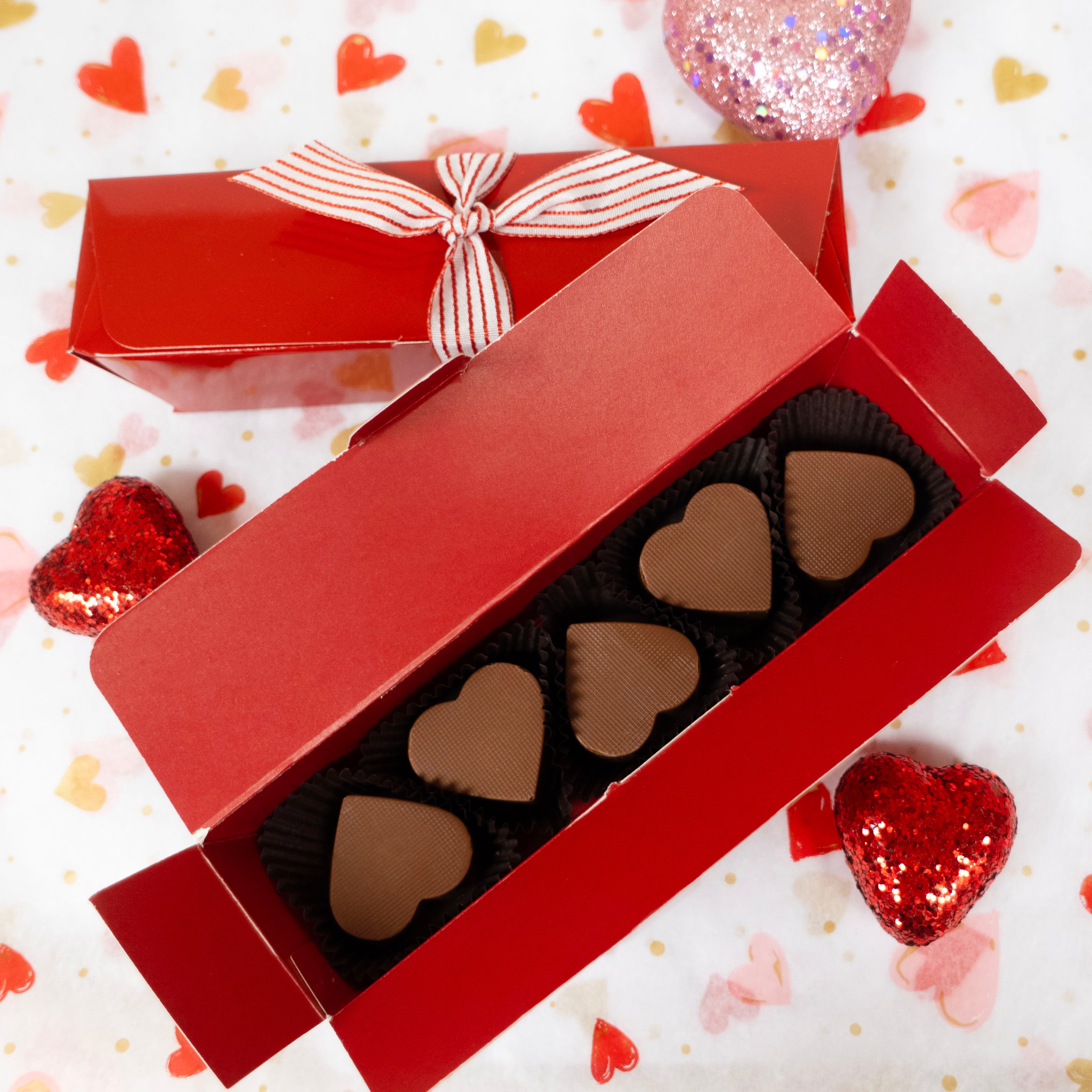Red box of 5 heart-shaped milk chocolates on a decorative background with hearts and sparkles.