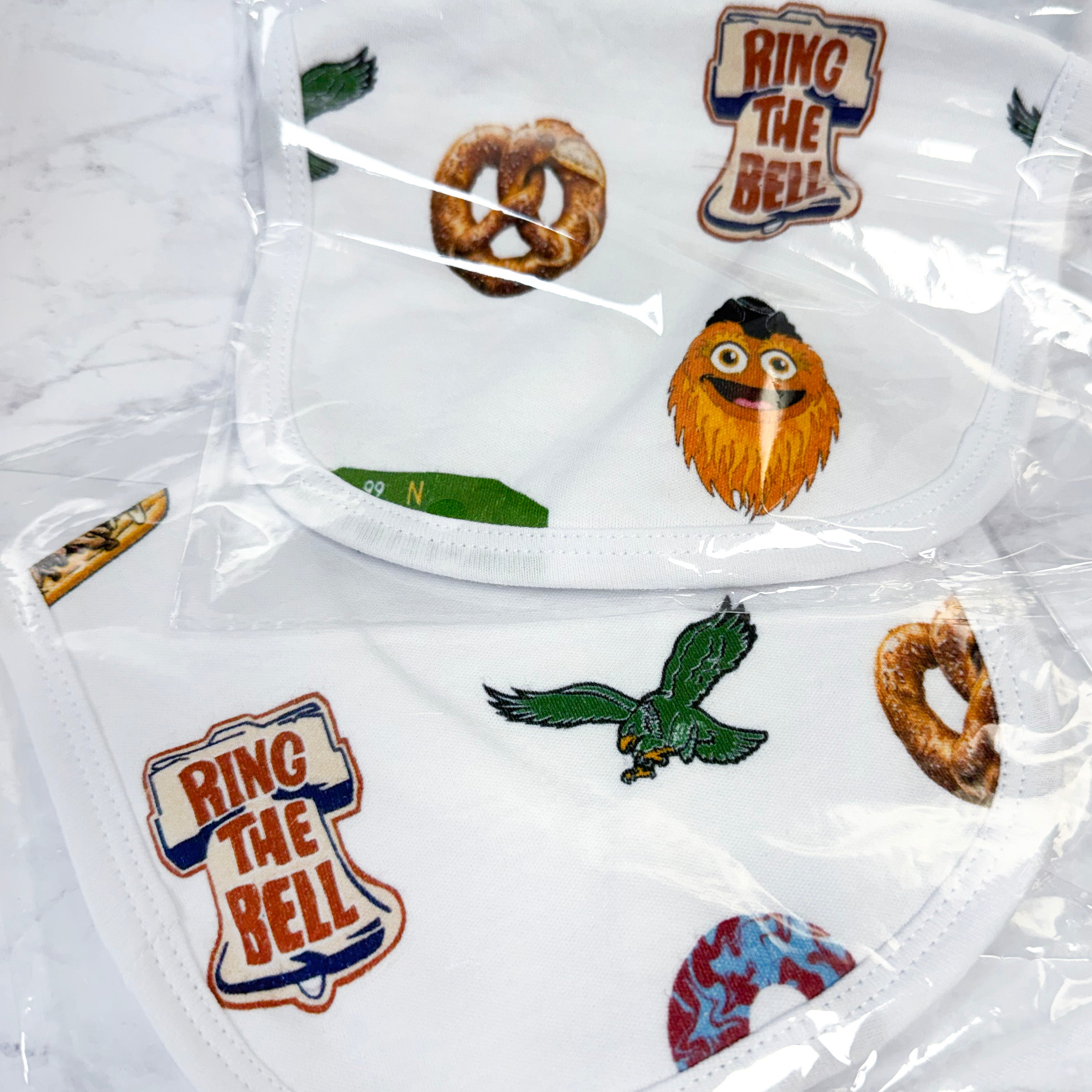 White baby bibs in clear bags with sports team logos and 'Ring the Bell' text on a white background