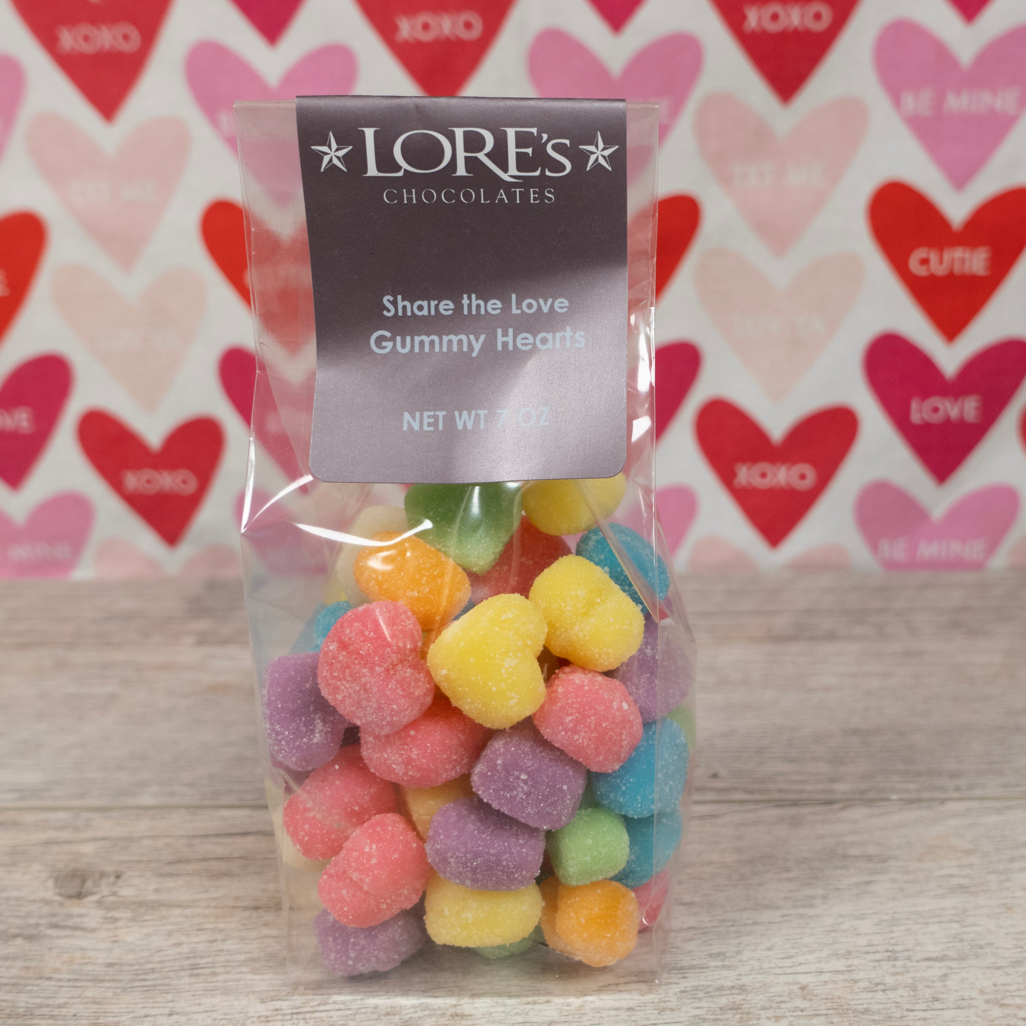 rainbow colored gummies in the shape of hearts for valentine's day pink, green, orange, purple, blue, yellow- label reads "Lore's Chocolates, Share the Love Gummy Hearts Net Wt 7 oz" 