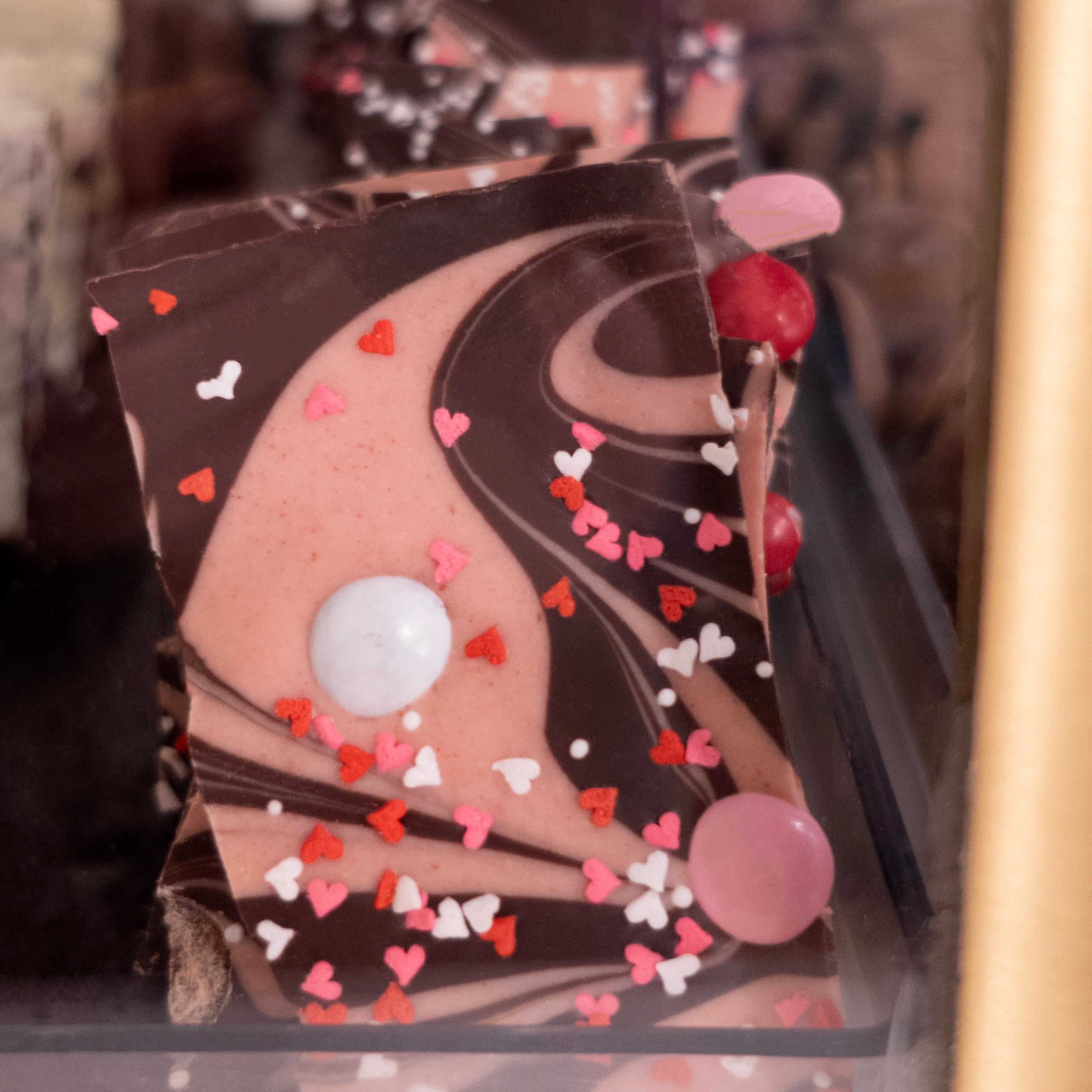 Close up of strawberry cheese cake pink swirl dark chocolate bark with white, red, and pink valentine's candies and hearts