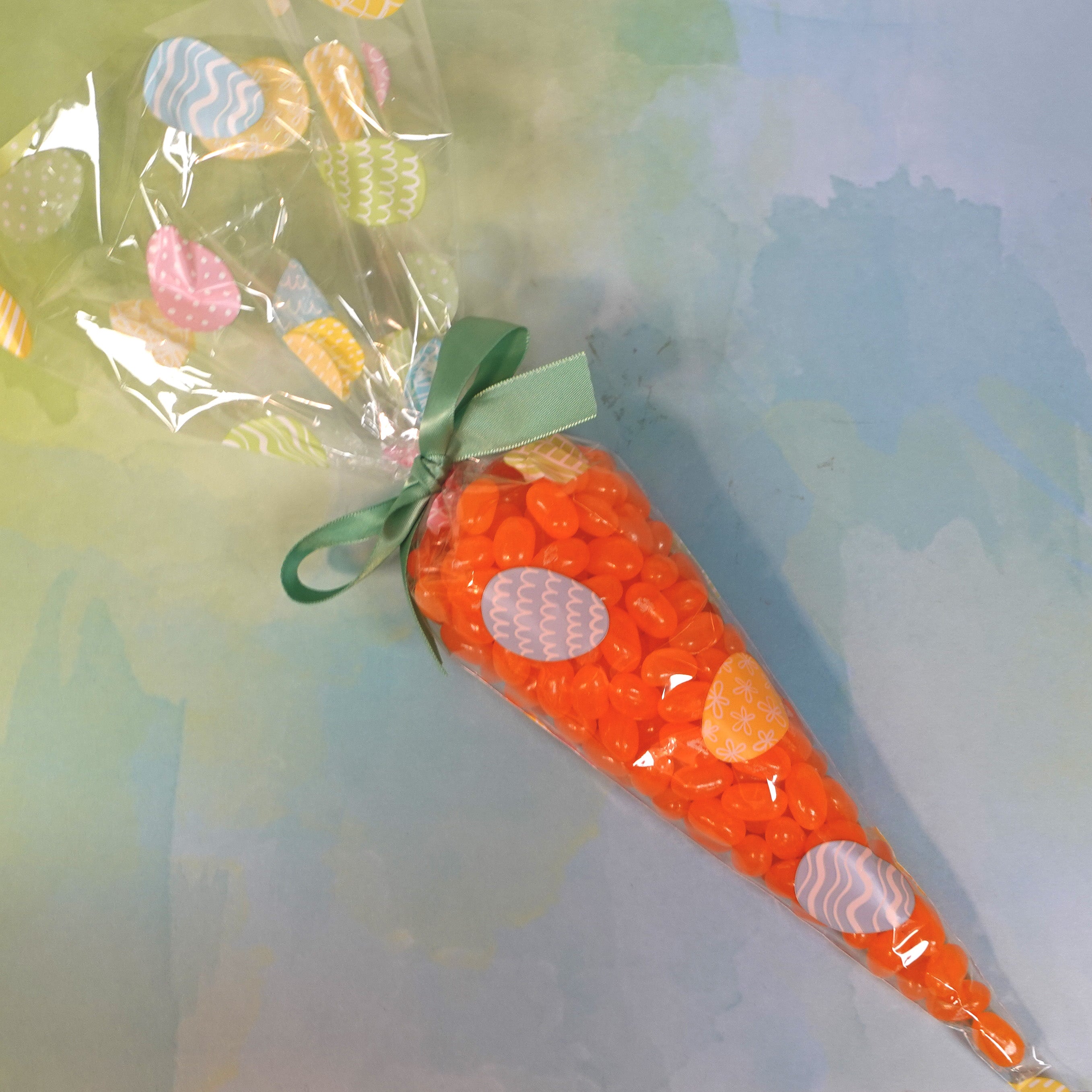 Orange colored, tangerine jelly beans packed in a cone back to resemble a carrot with sage green ribbon and designed easter eggs